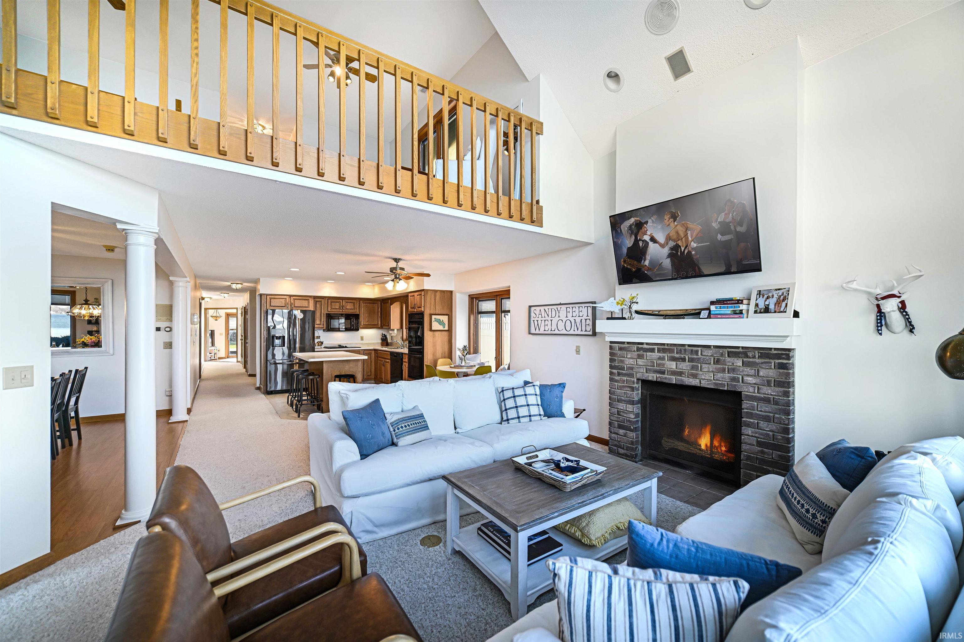 Living room featuring decorative columns, a brick fireplace, light colored carpet, recessed lighting, and high vaulted ceiling
