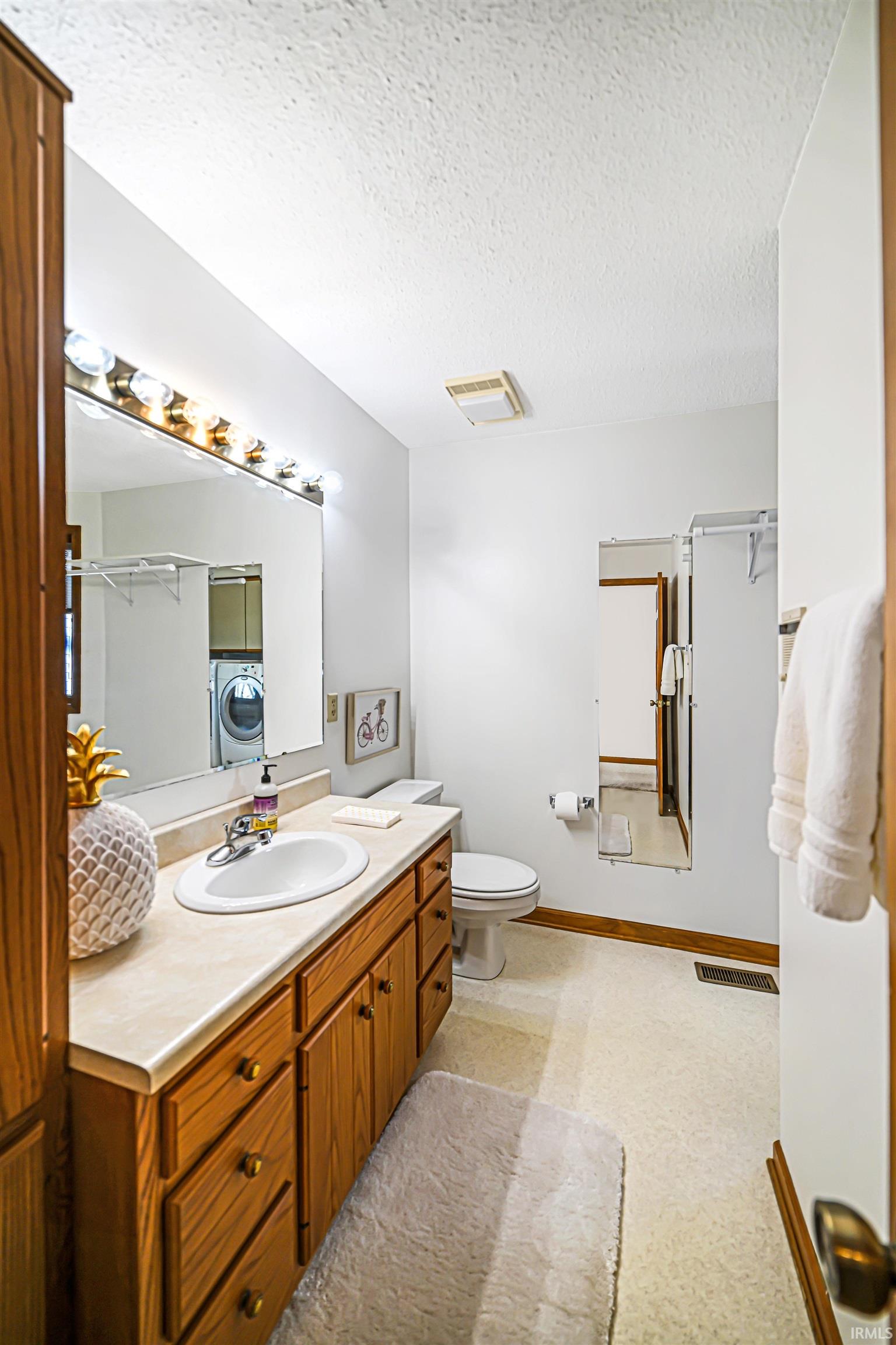 Full bath with vanity, a textured ceiling, and washer / dryer