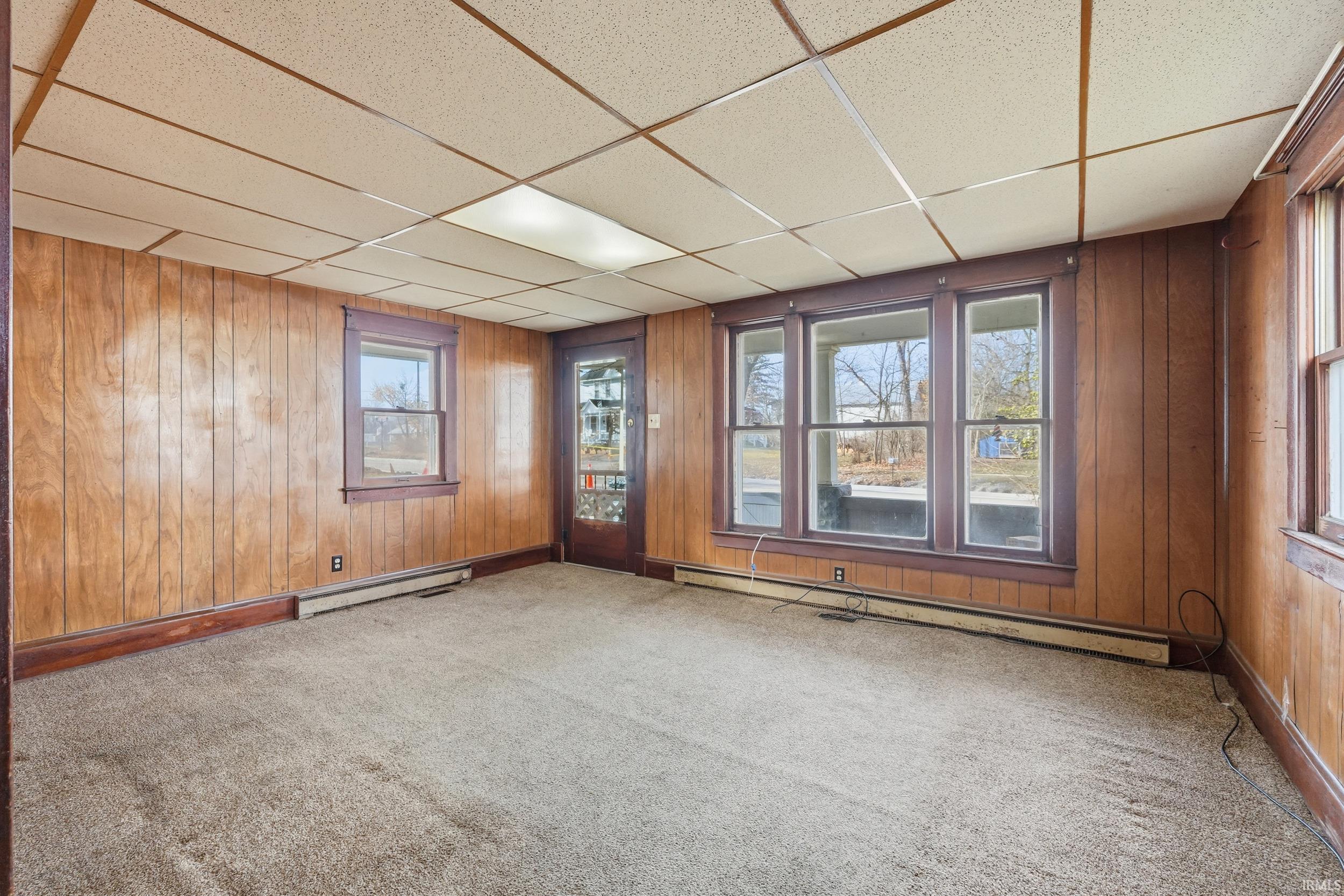 Spare room with a paneled ceiling, baseboard heating, wood walls, plenty of natural light, and carpet