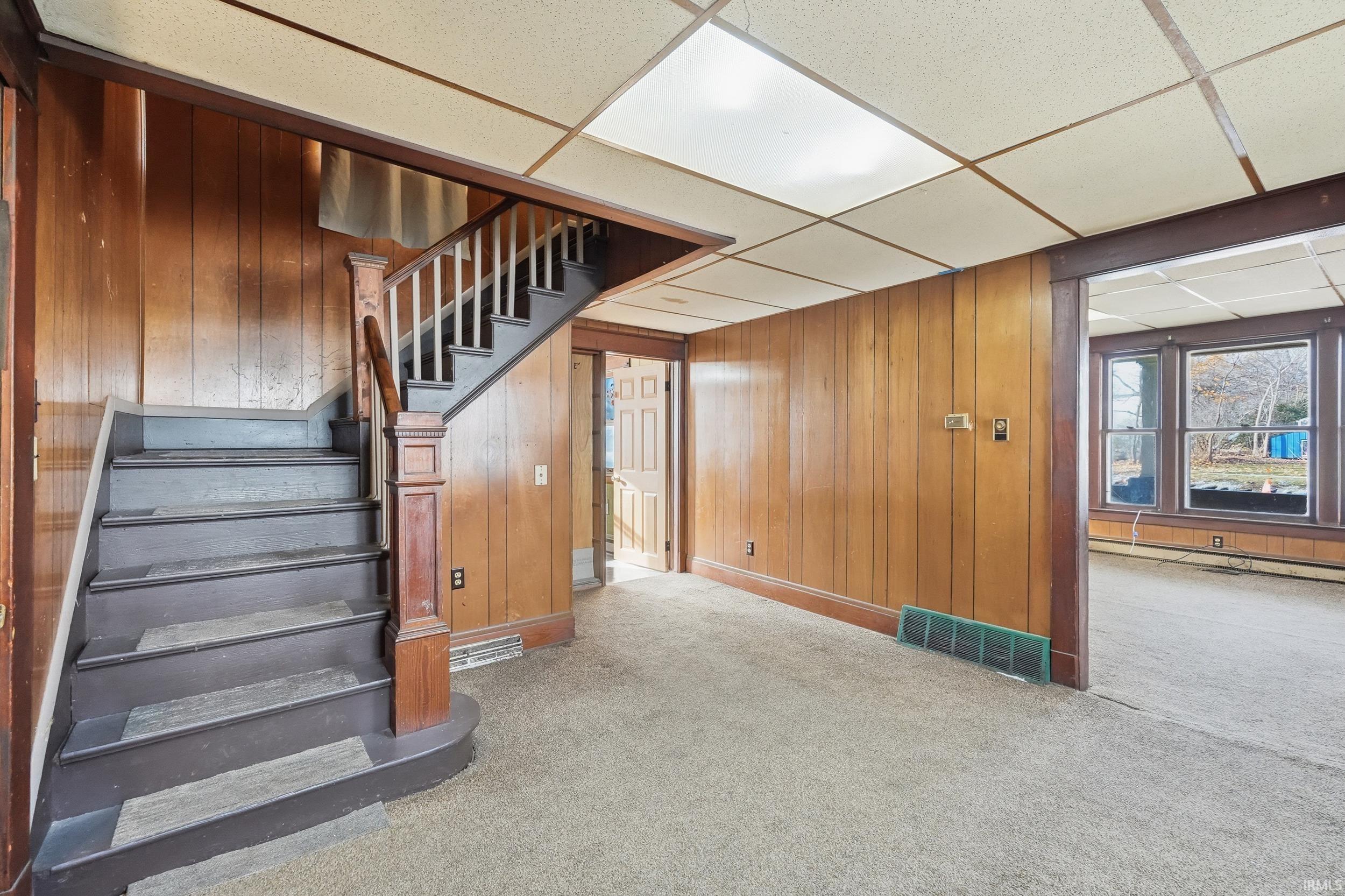 Stairway featuring a drop ceiling, wooden walls, carpet flooring, and a baseboard radiator