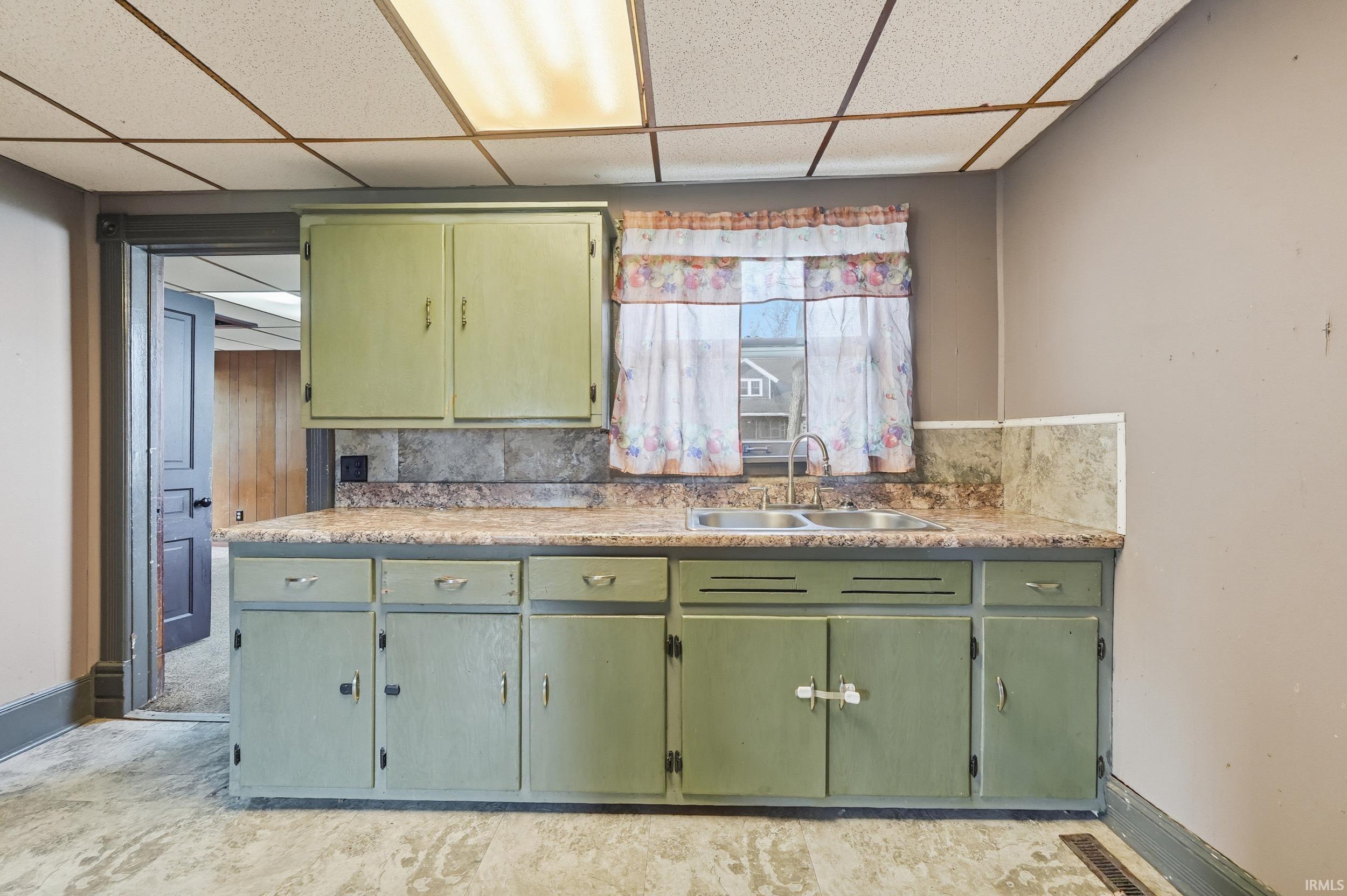 Kitchen with green cabinetry, a drop ceiling, and light countertops