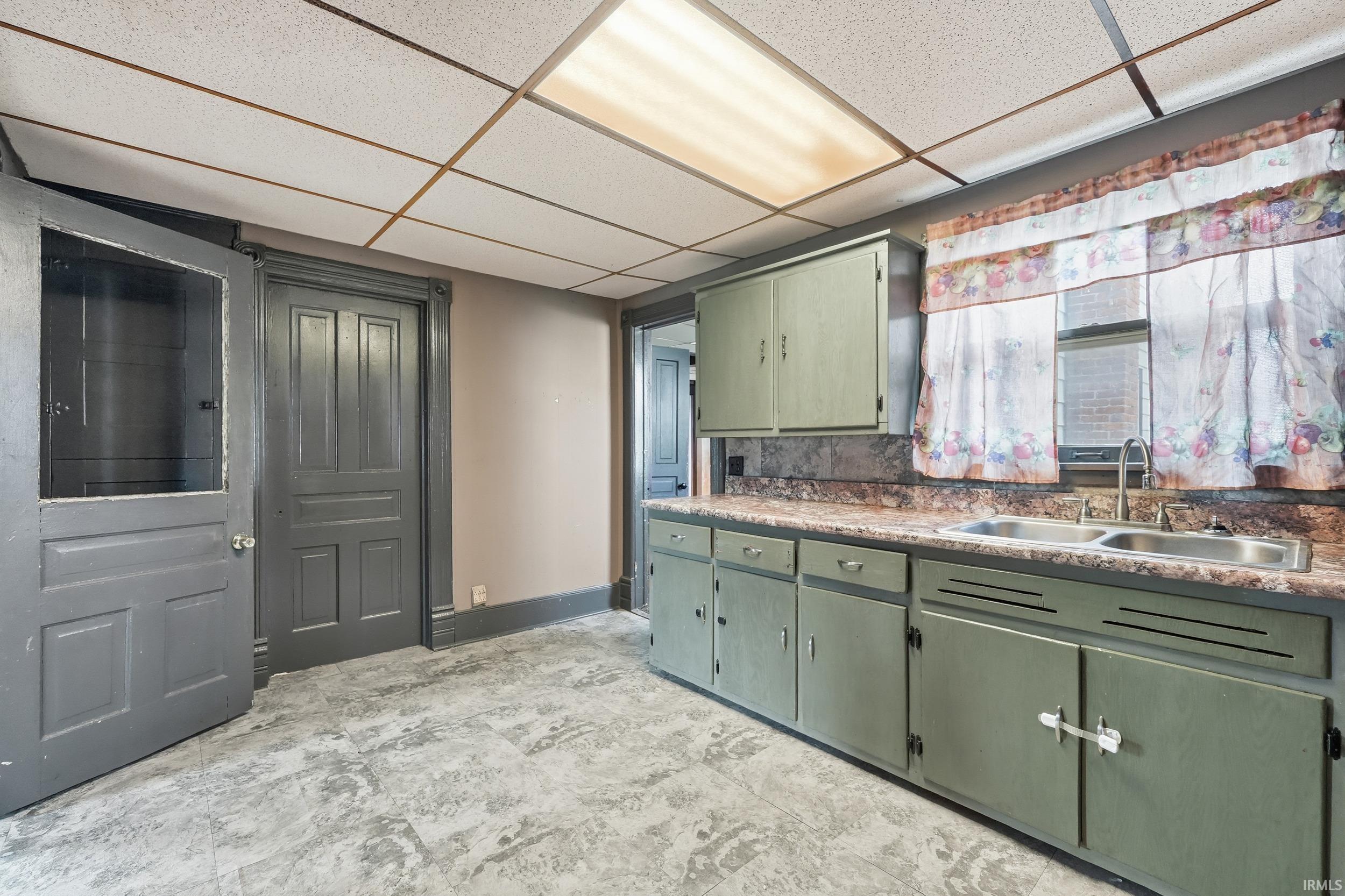 Kitchen with green cabinetry, a drop ceiling, and light countertops