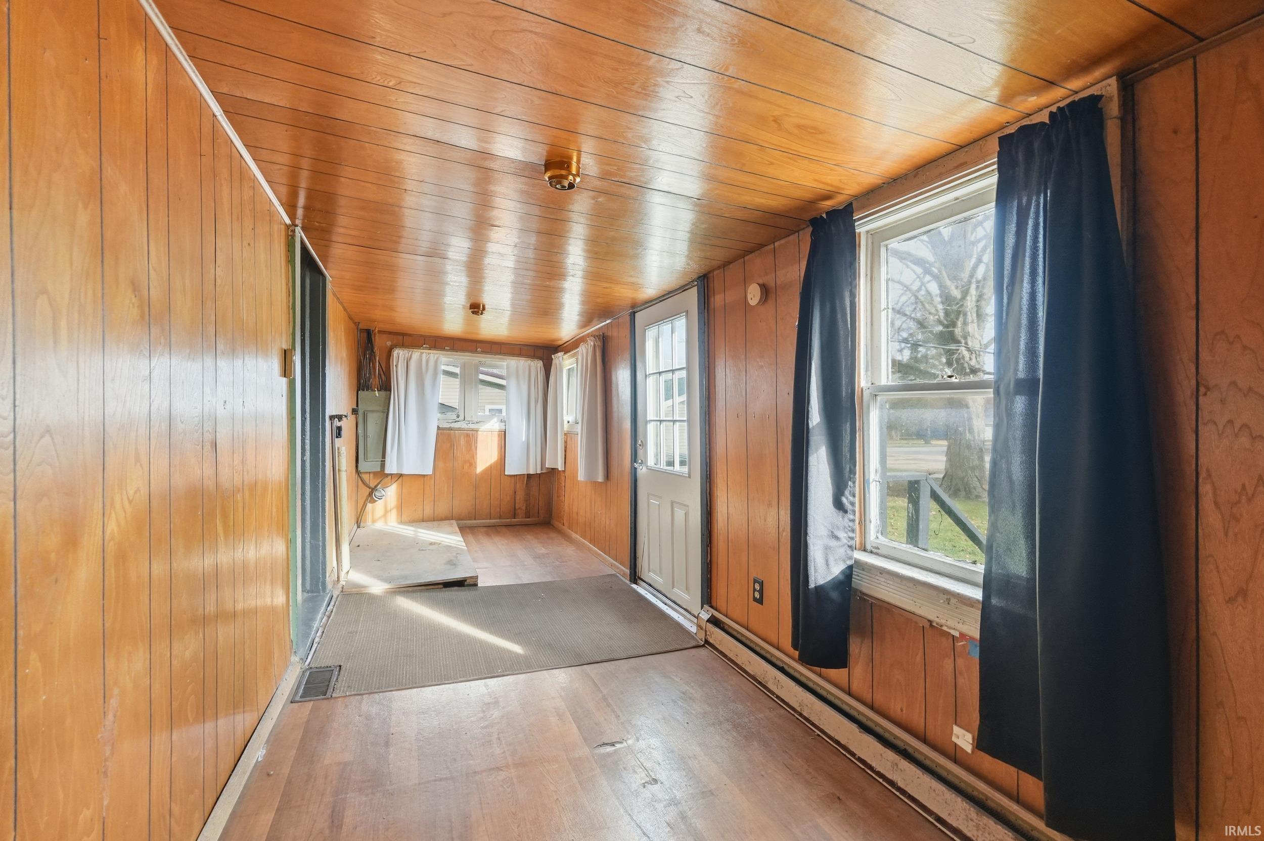 Hall featuring baseboard heating, wooden ceiling, wooden walls, and wood-type flooring