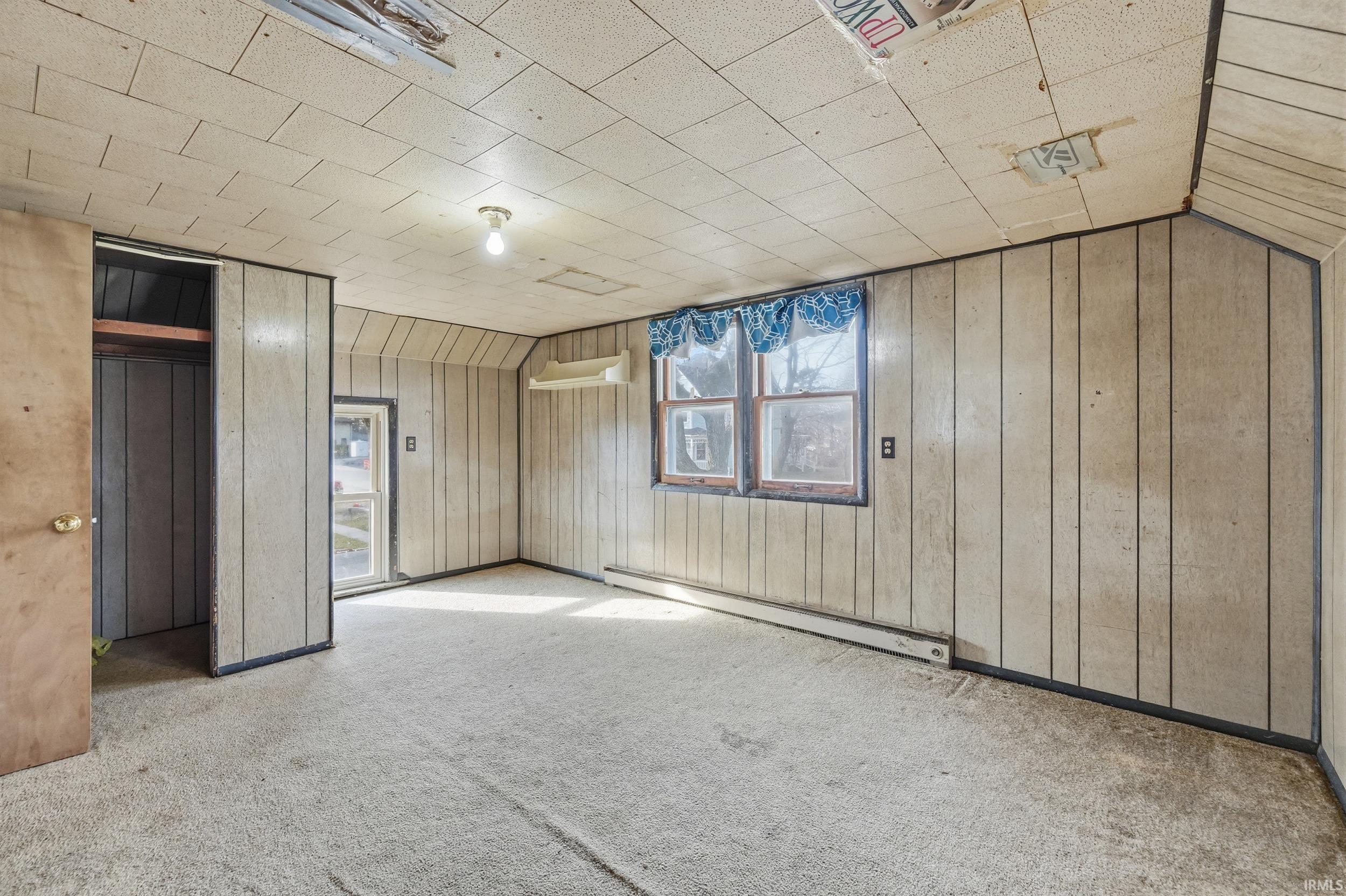 Unfurnished bedroom featuring a baseboard heating unit, carpet flooring, wood walls, lofted ceiling, and a closet