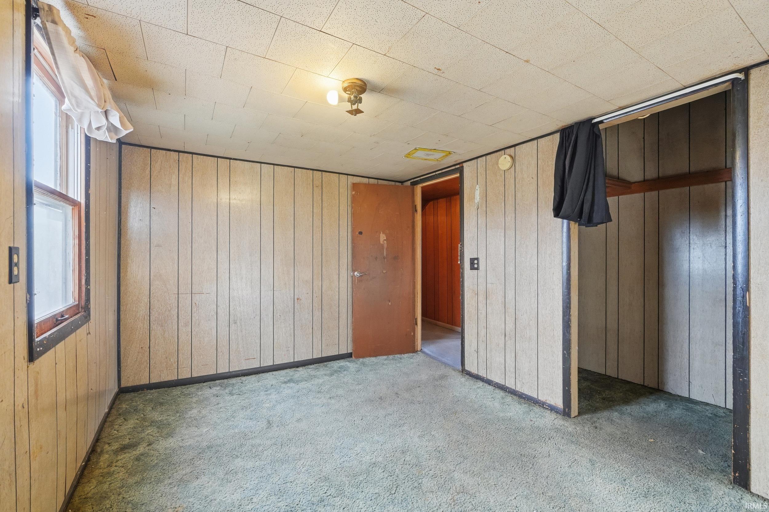 Unfurnished bedroom featuring wooden walls, carpet floors, and a closet