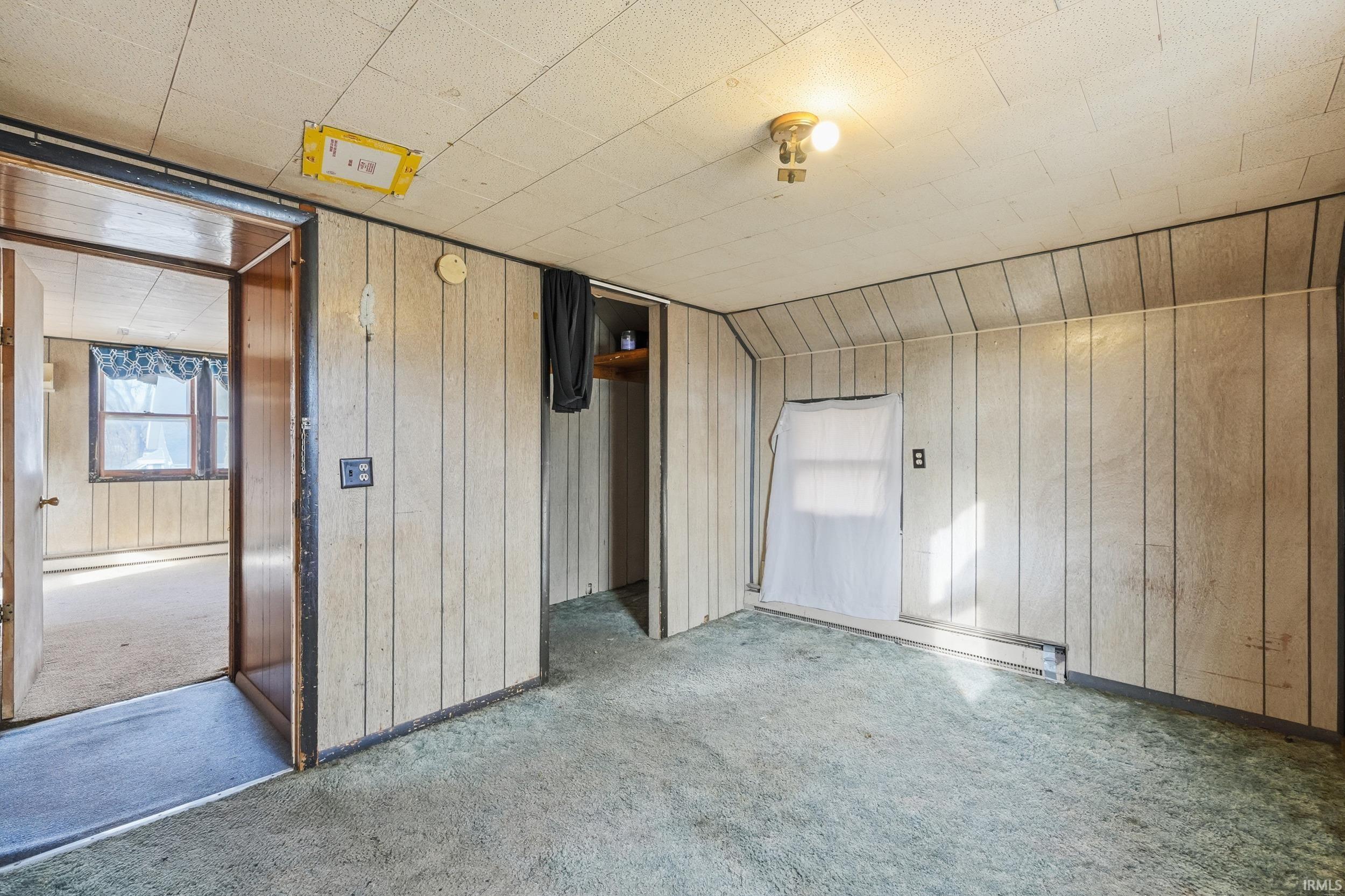 Unfurnished bedroom with carpet flooring, wood walls, and vaulted ceiling