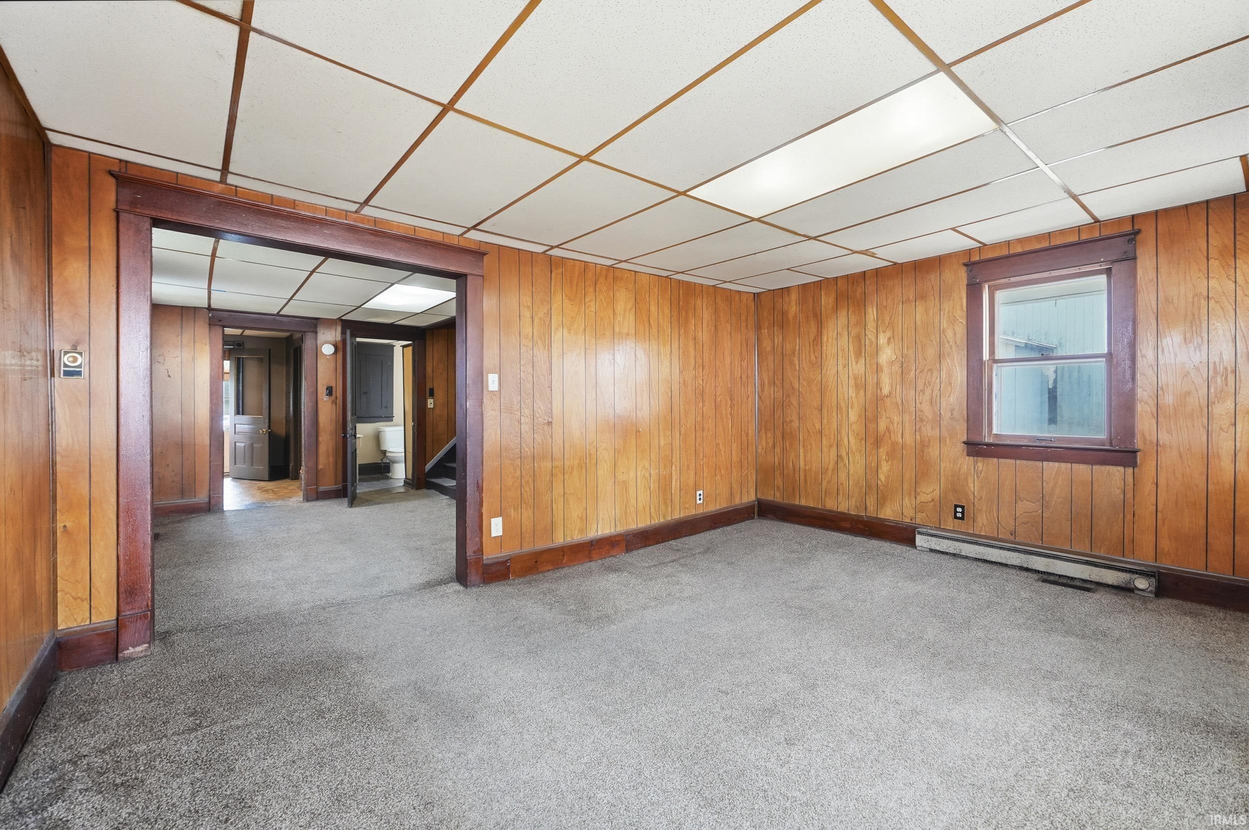 Unfurnished room with carpet floors, wooden walls, a paneled ceiling, and stairs