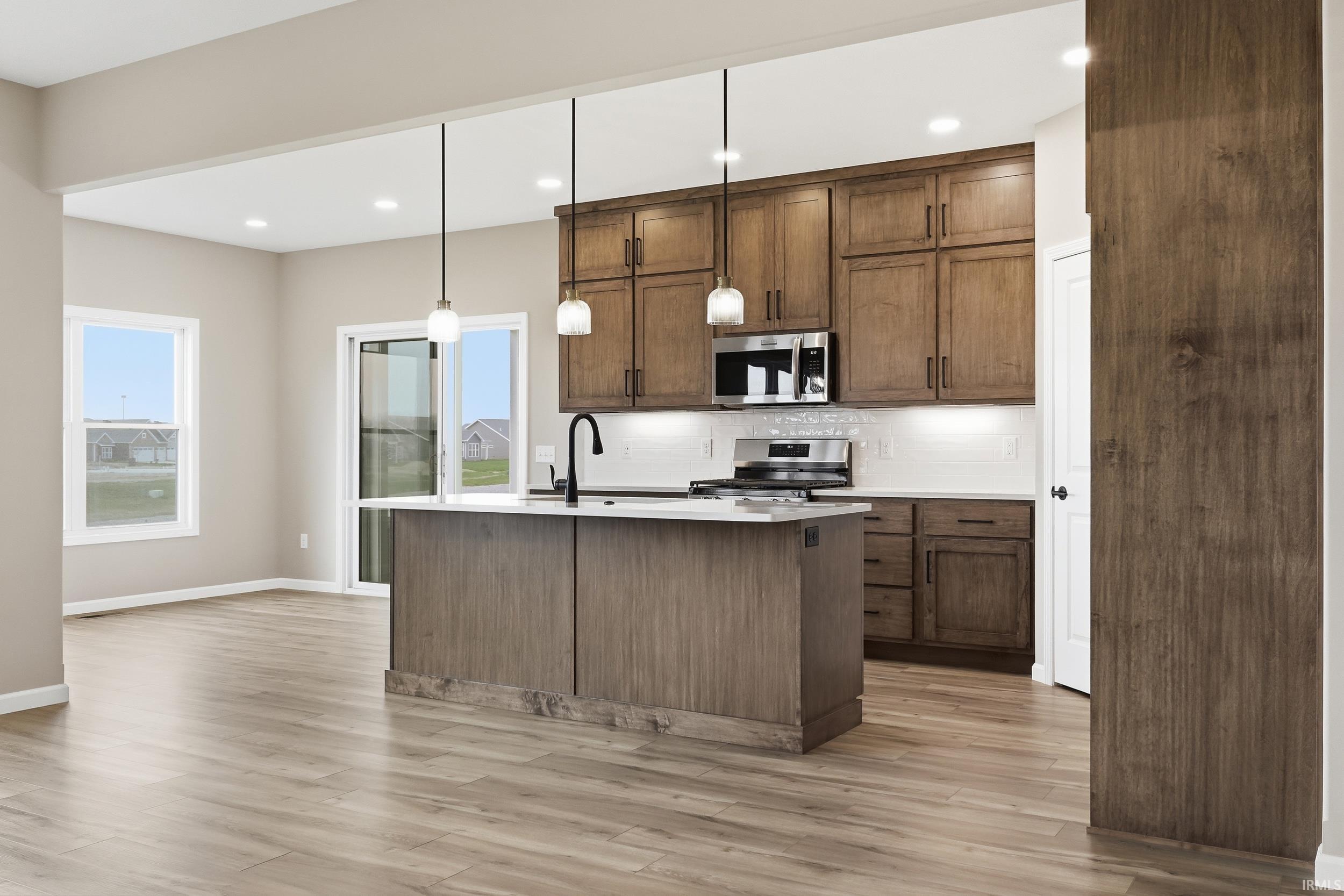Kitchen featuring tasteful backsplash, stainless steel appliances, light wood-type flooring, and a center island with sink