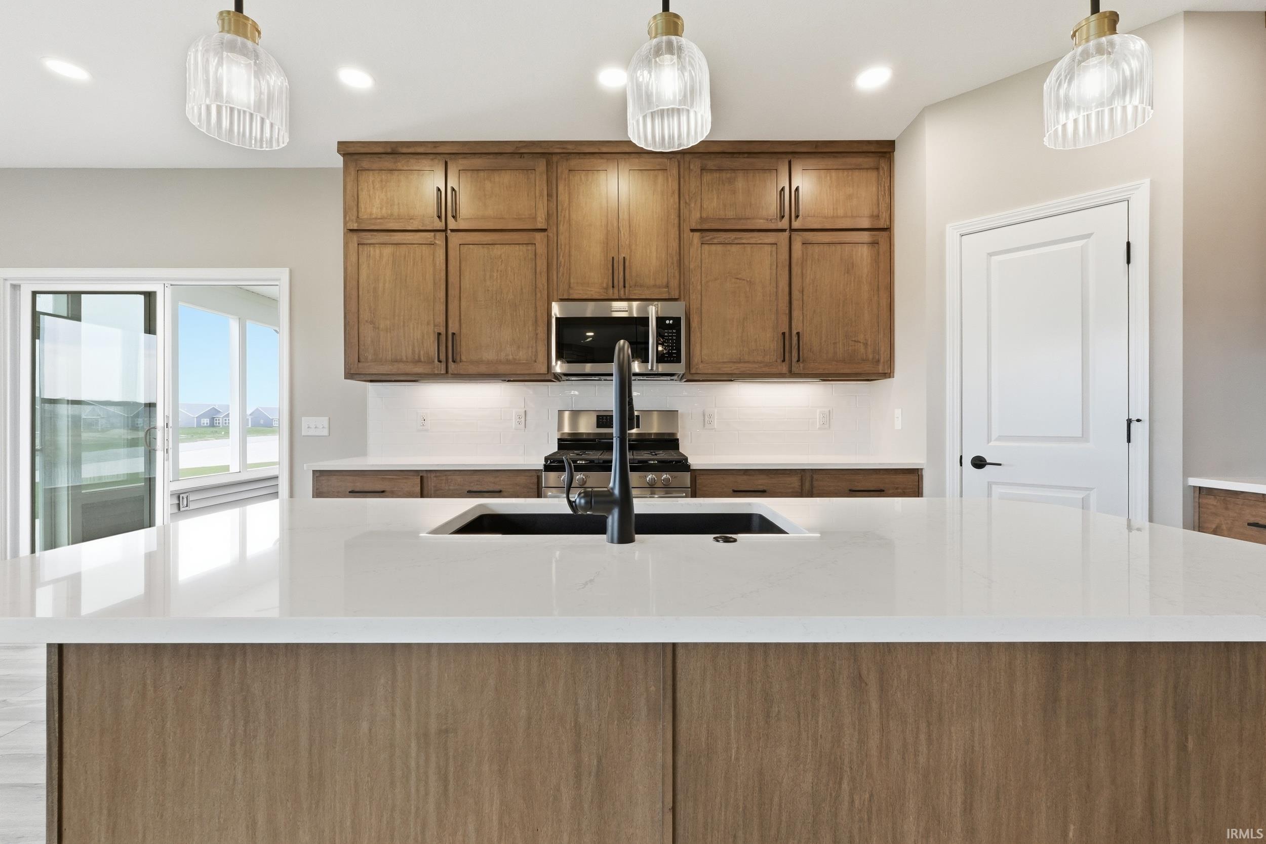 Kitchen featuring wood finish cabinetry, pendant lighting, light stone counters, and stainless steel appliances