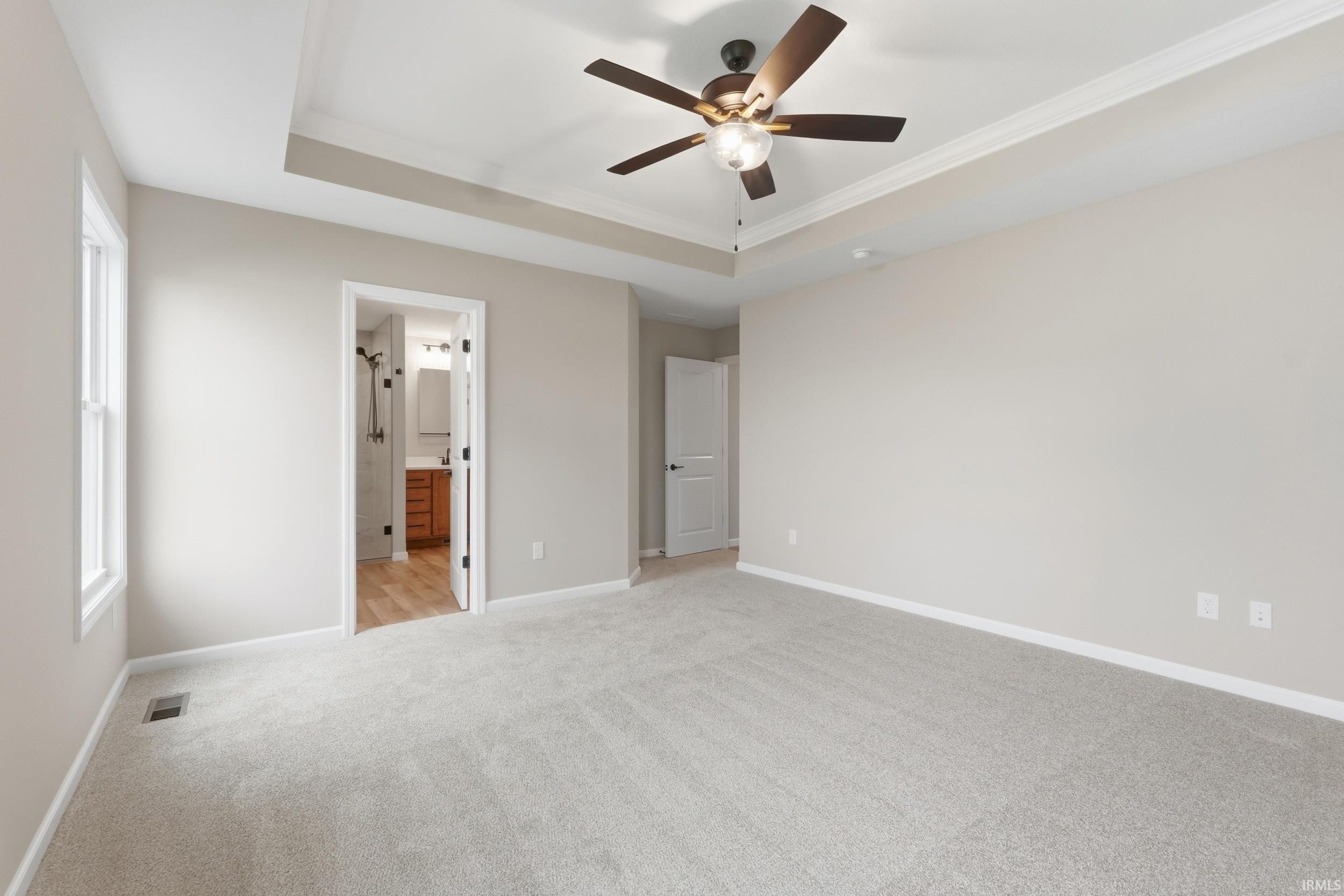 Unfurnished bedroom with light carpet, a tray ceiling, a ceiling fan, crown molding, and connected bathroom