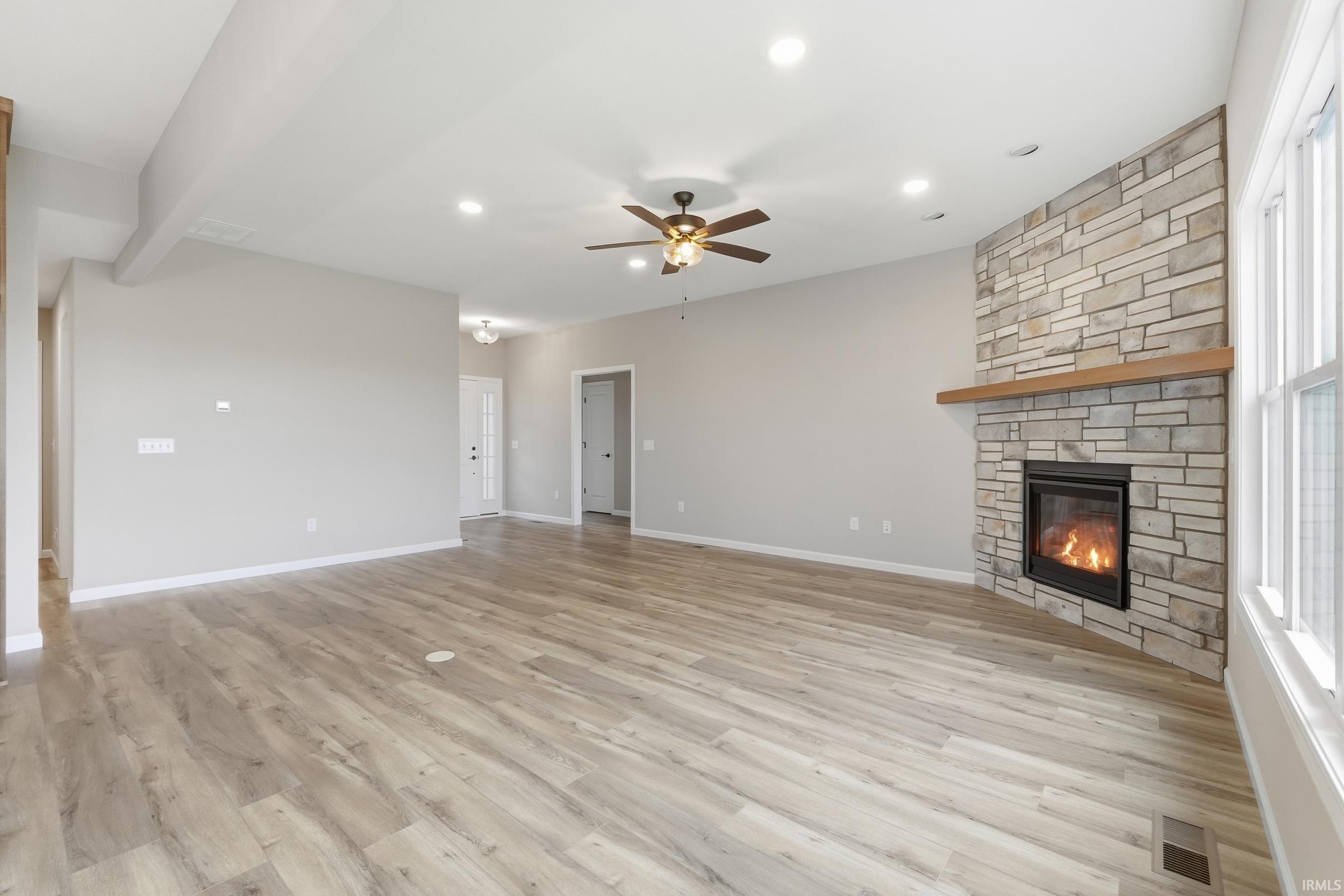Unfurnished living room with a stone fireplace, a ceiling fan, light wood-style flooring, and recessed lighting