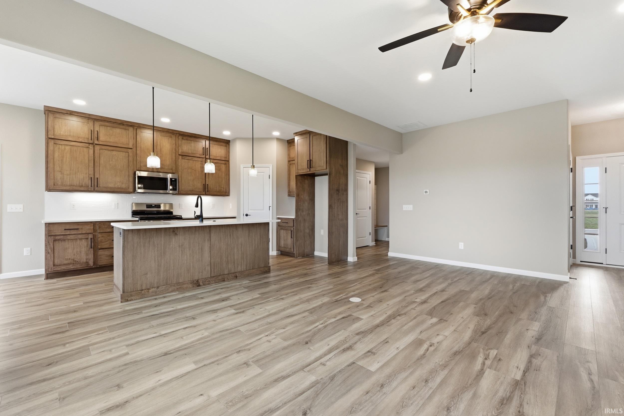 Kitchen featuring wood finish cabinetry, a kitchen island with sink, open floor plan, ceiling fan, and stainless steel appliances