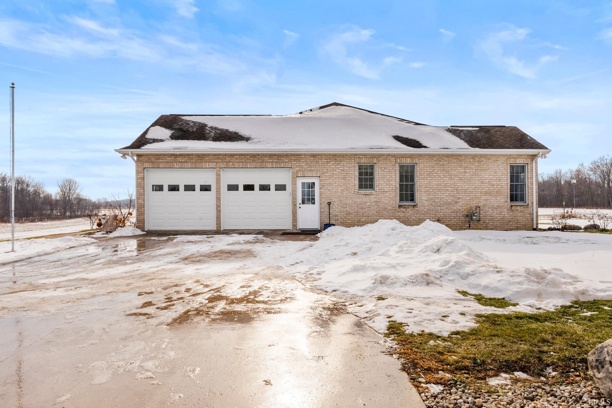 View of snowy exterior with brick siding, a garage, and driveway