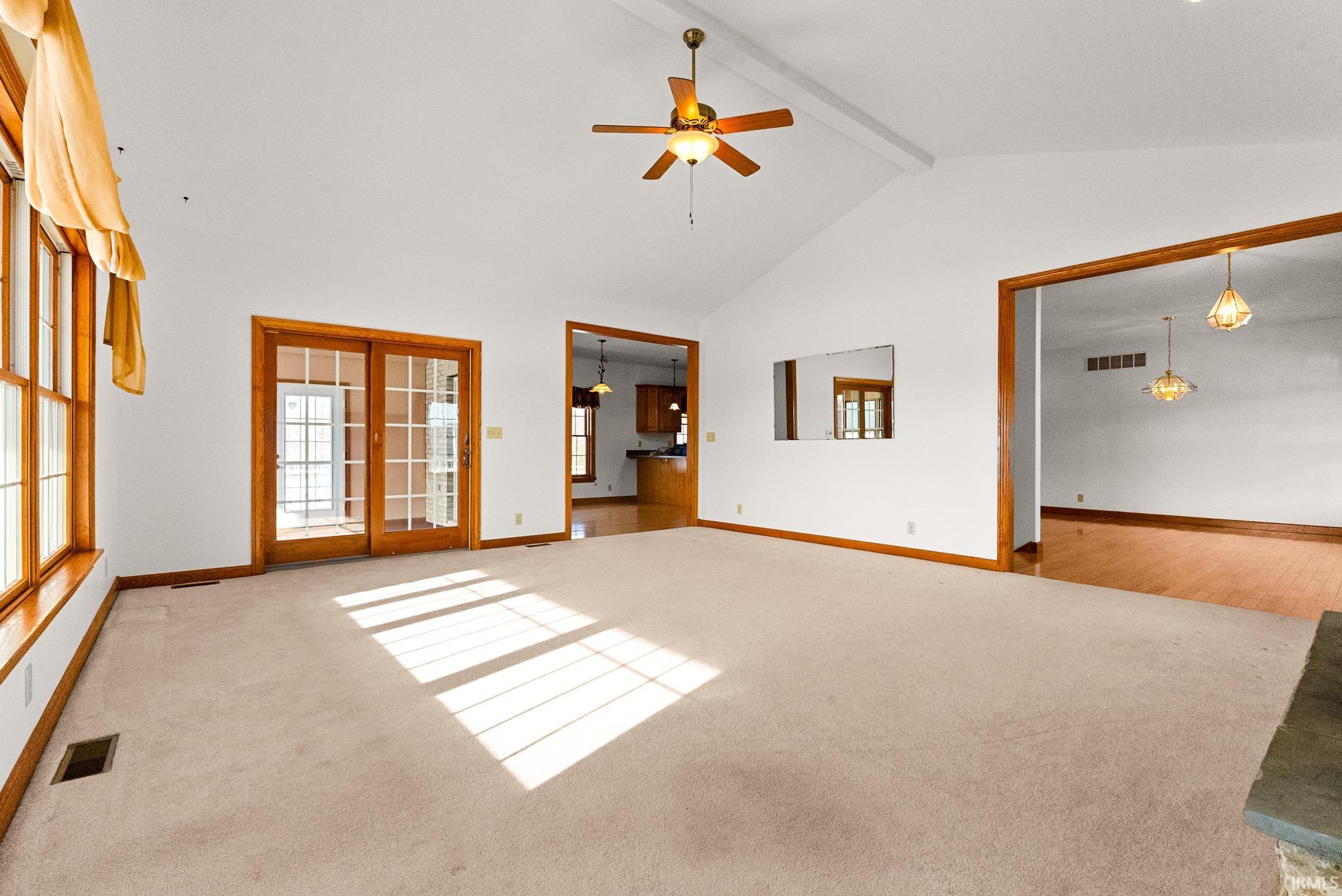 Unfurnished living room with beam ceiling, ceiling fan, light carpet, and high vaulted ceiling