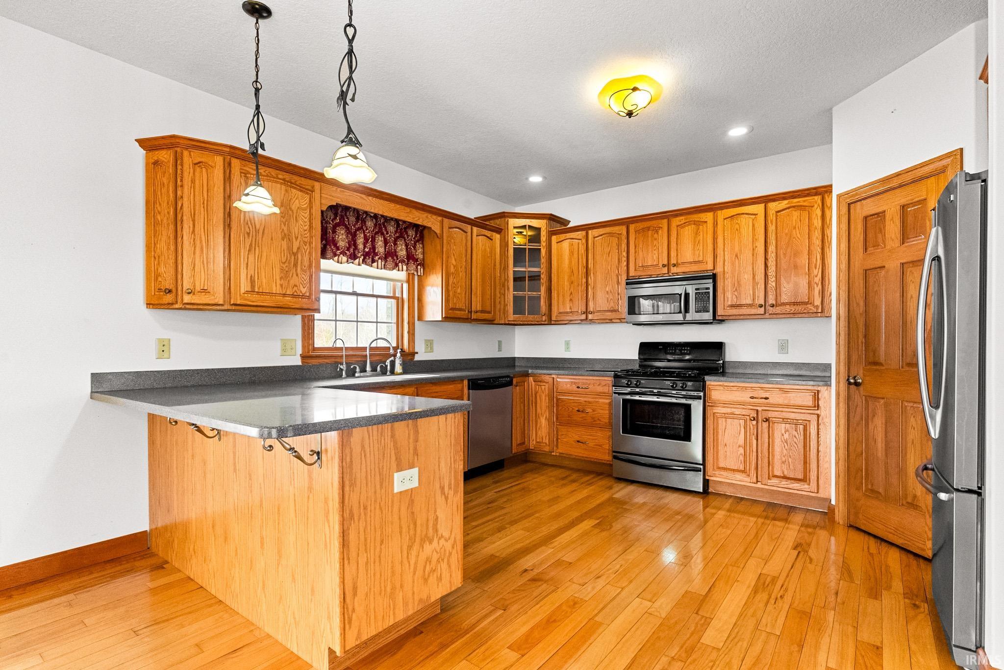 Kitchen with pendant lighting, appliances with stainless steel finishes, a peninsula, brown cabinetry, and a kitchen breakfast bar