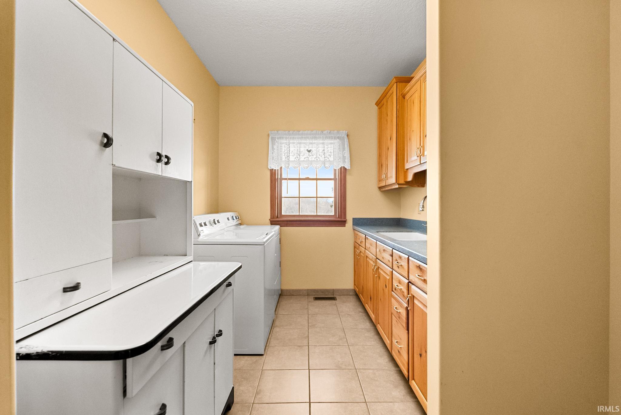 Washroom with cabinet space, light tile patterned floors, washer and clothes dryer, and a textured ceiling