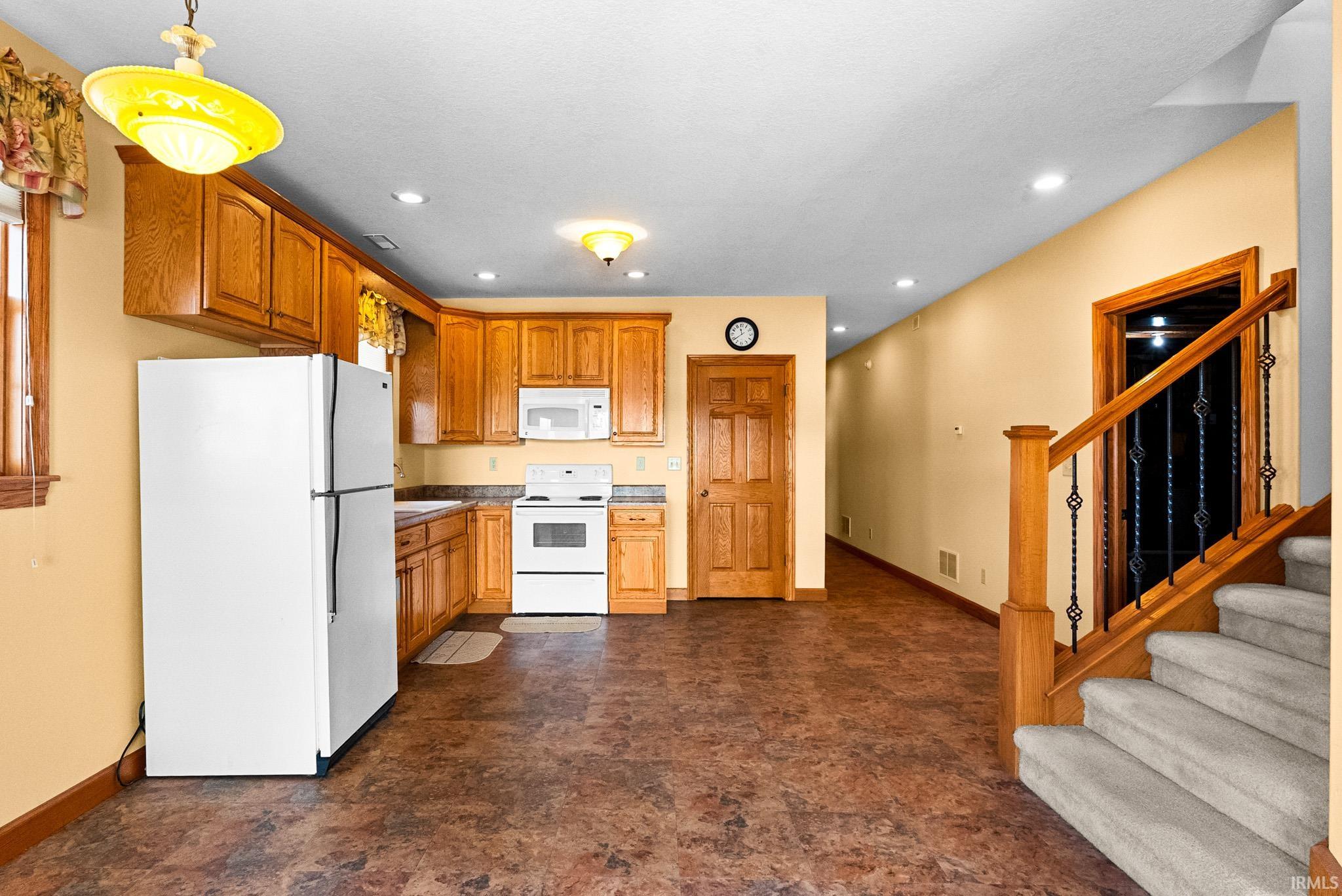 Kitchen with white appliances, recessed lighting, brown cabinets, and hanging light fixtures