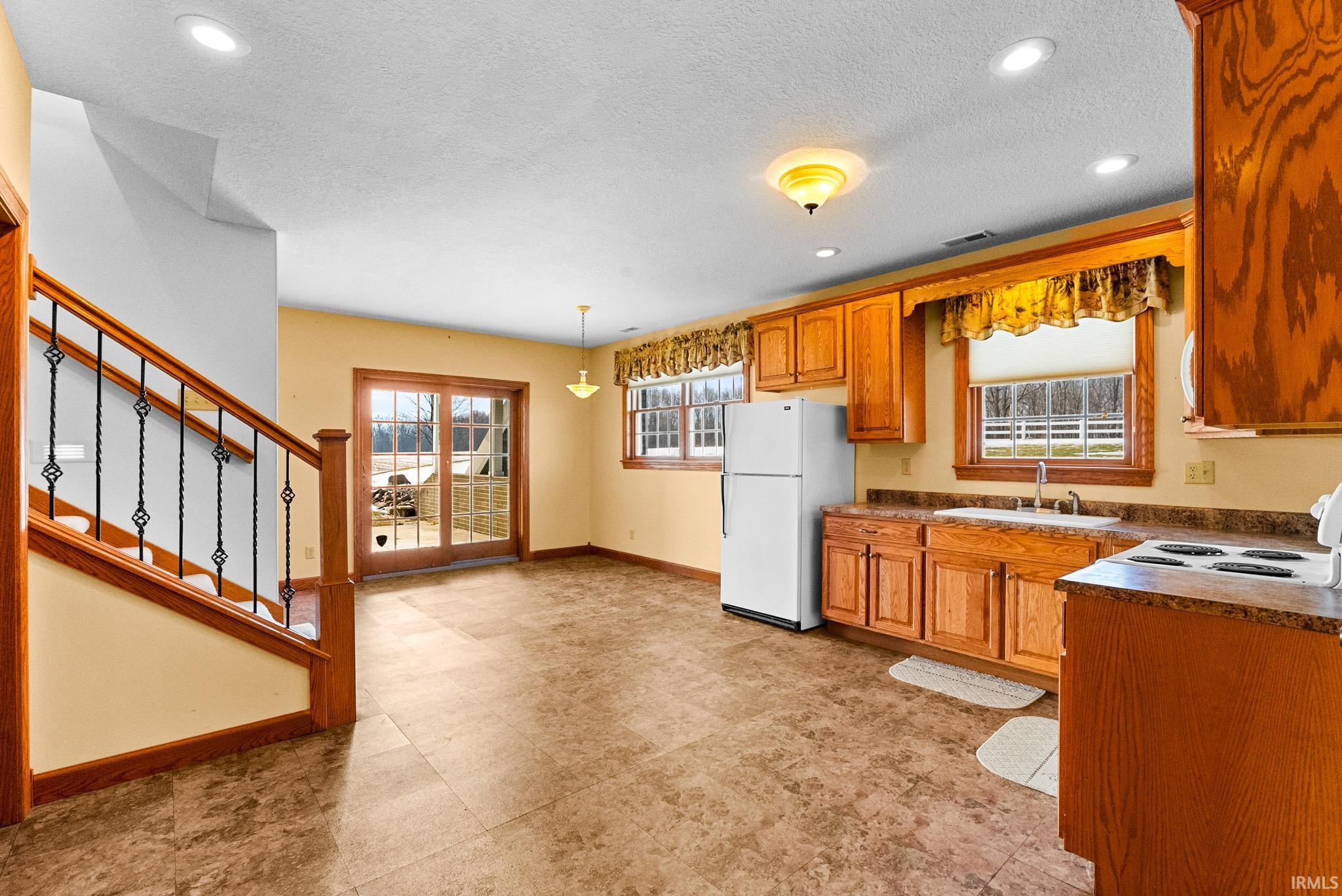 Kitchen with brown cabinets, white appliances, dark countertops, recessed lighting, and a textured ceiling