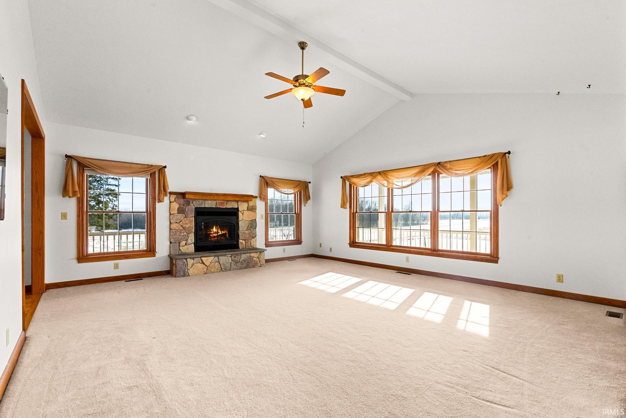 Unfurnished living room with beam ceiling, a ceiling fan, a fireplace, light colored carpet, and high vaulted ceiling