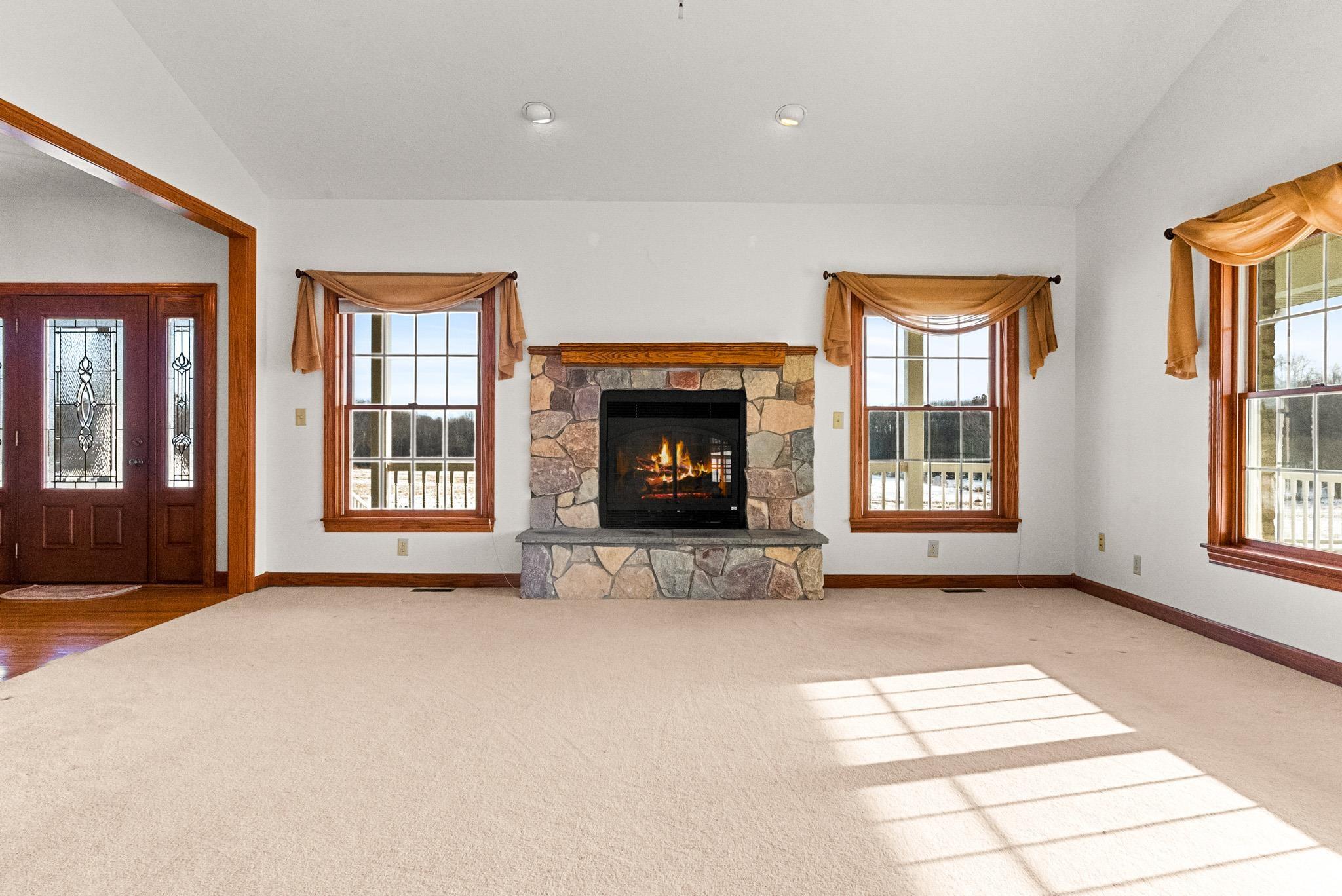 Unfurnished living room with vaulted ceiling, a fireplace, healthy amount of natural light, and carpet flooring