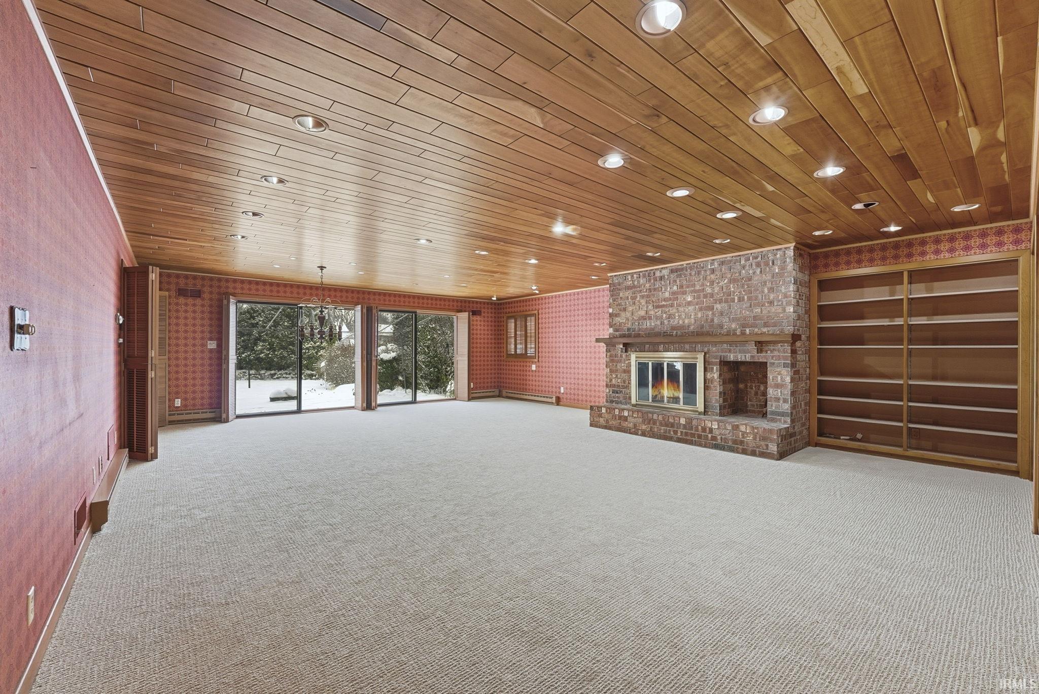 Unfurnished living room featuring wooden ceiling, light carpet, and a brick fireplace