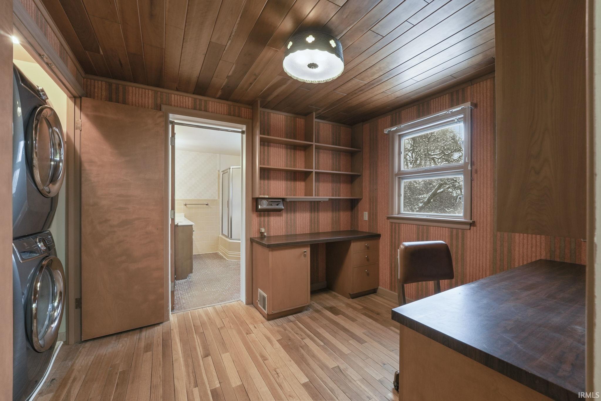 Unfurnished office featuring stacked washing machine and dryer, light wood-type flooring, wooden ceiling, and wooden walls