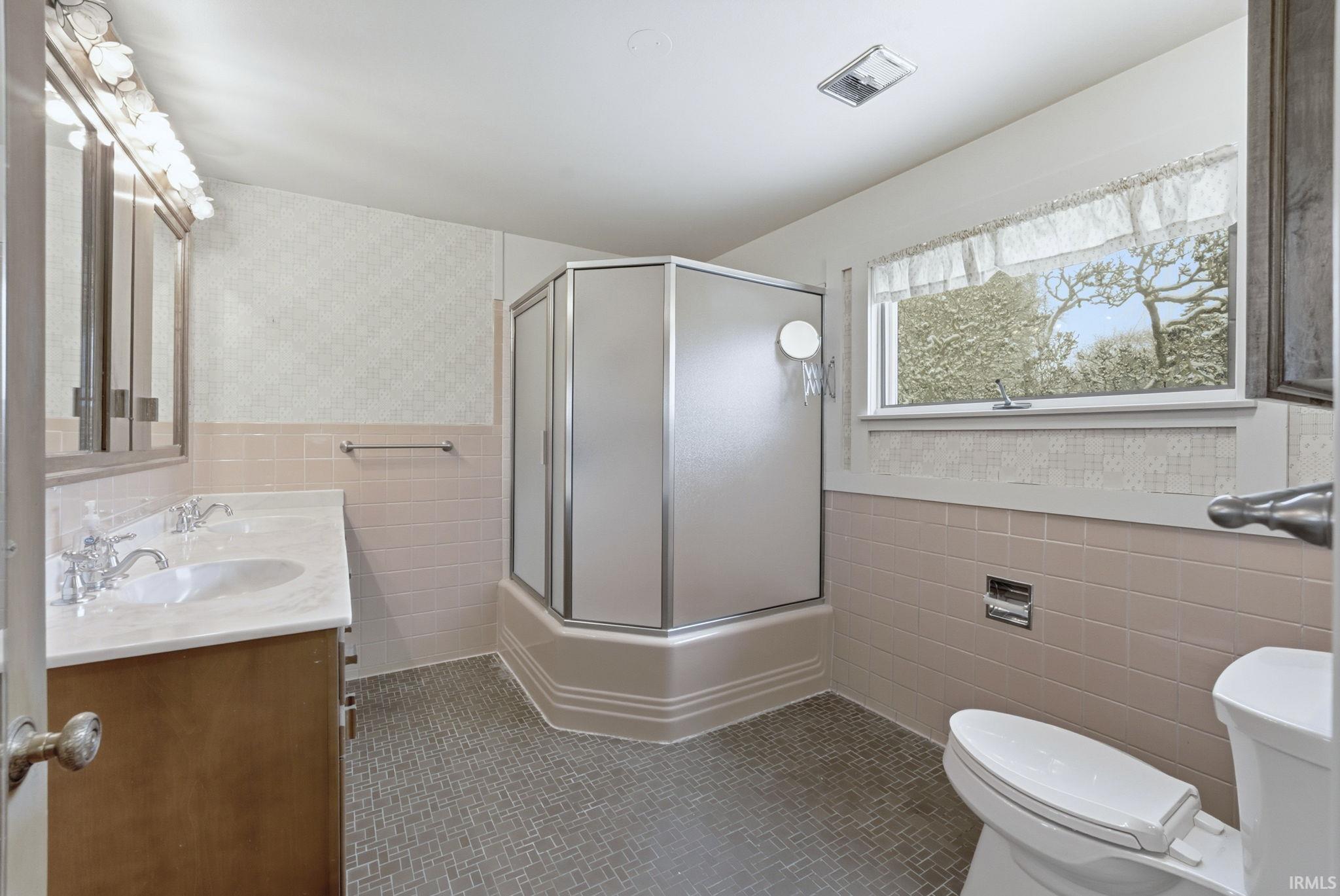 Bathroom featuring double vanity, tile walls, a wainscoted wall, enclosed tub / shower combo, and tile patterned floors