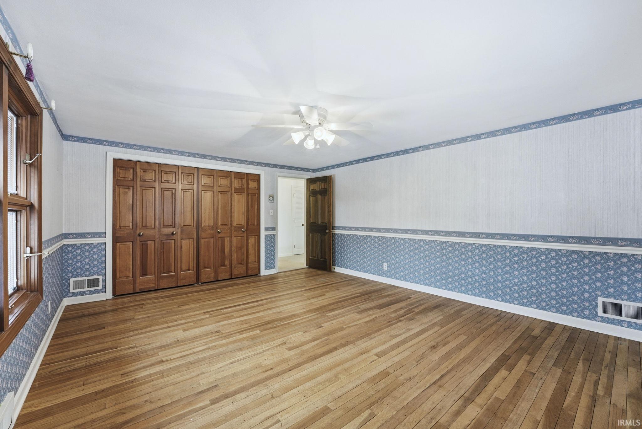 Unfurnished bedroom with wallpapered walls, light wood-style floors, a ceiling fan, and a closet