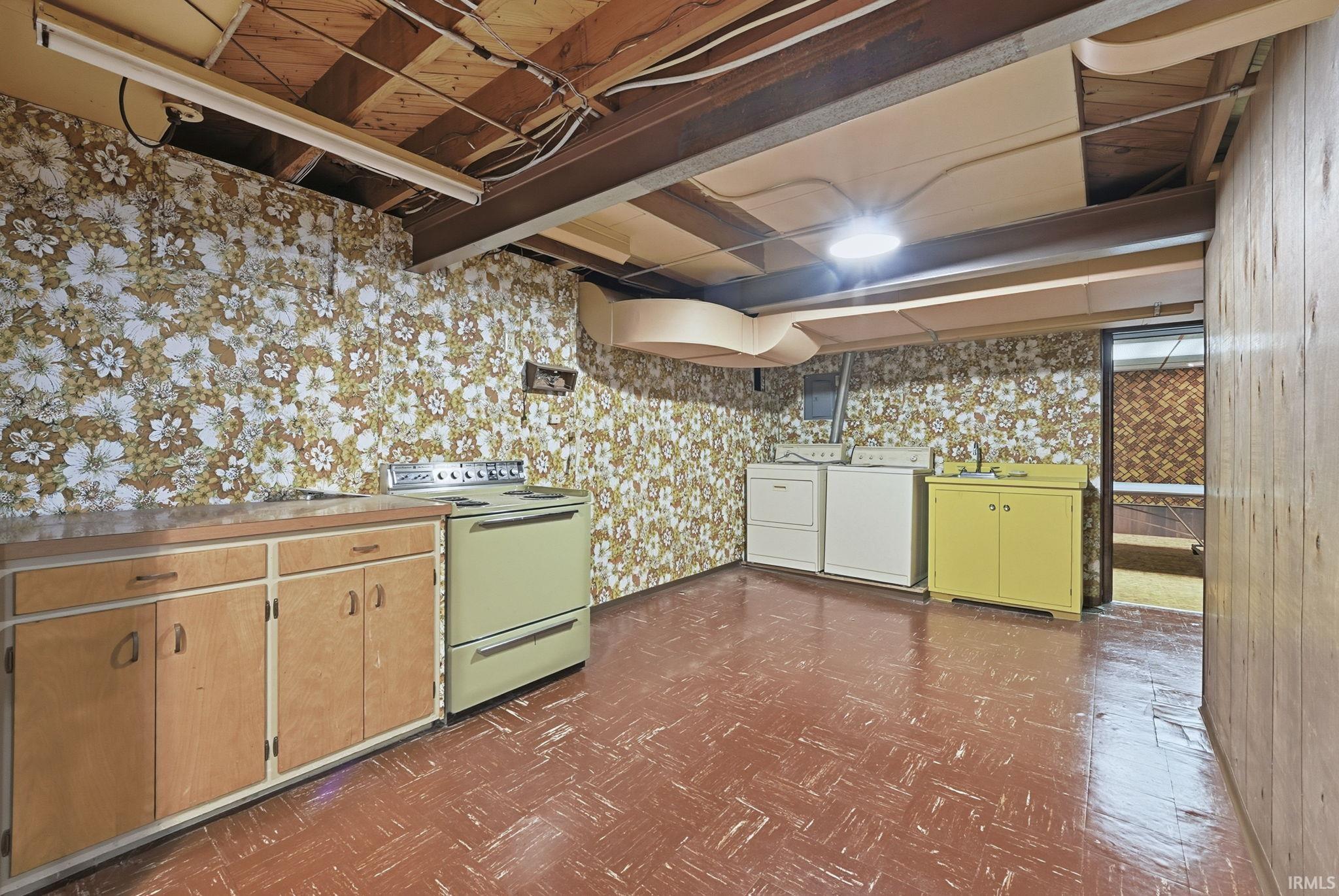 Kitchen with dark floors, range with electric stovetop, washer and dryer, light countertops, and wallpapered walls