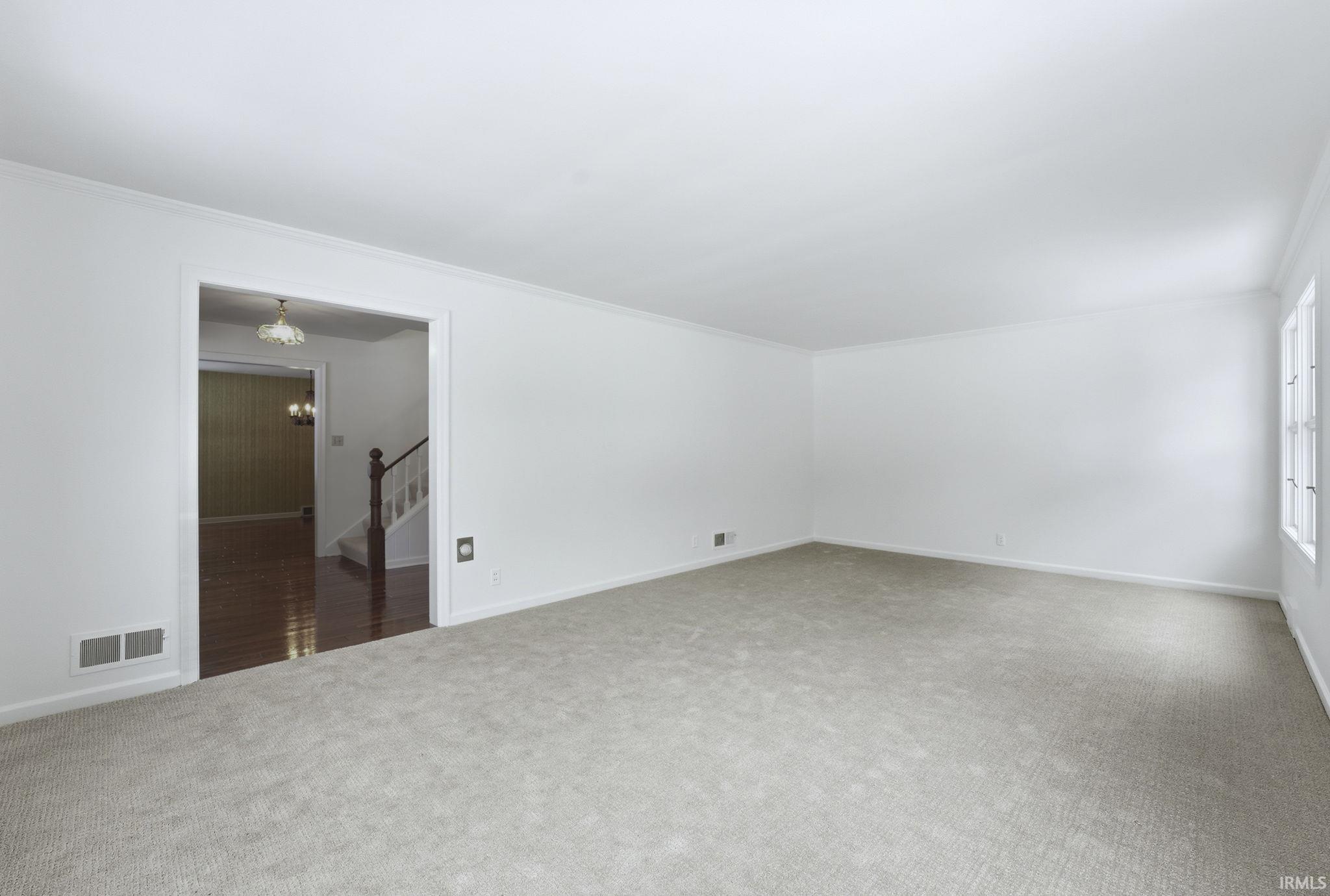 Carpeted empty room featuring a chandelier, stairway, and crown molding