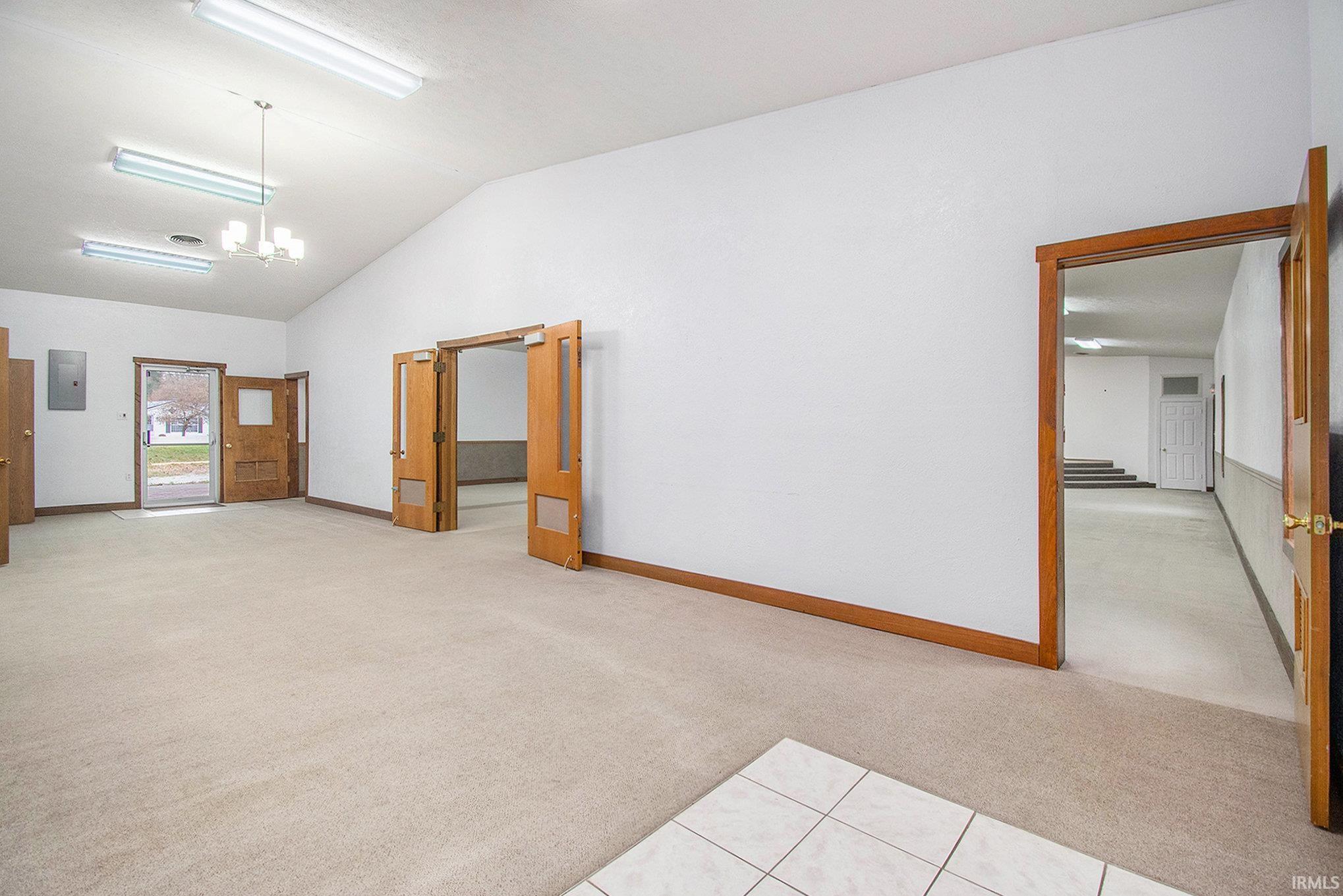 Empty room featuring light carpet, vaulted ceiling, electric panel, a chandelier, and light tile patterned floors