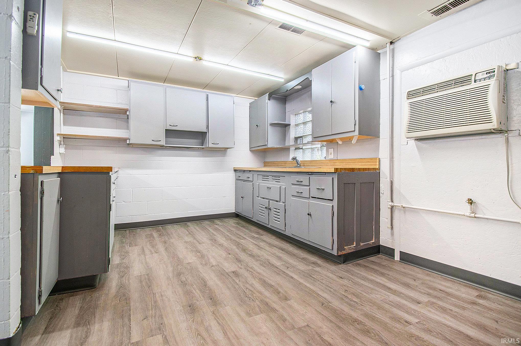 Kitchen with open shelves, gray cabinetry, an AC wall unit, light wood-style floors, and concrete block wall