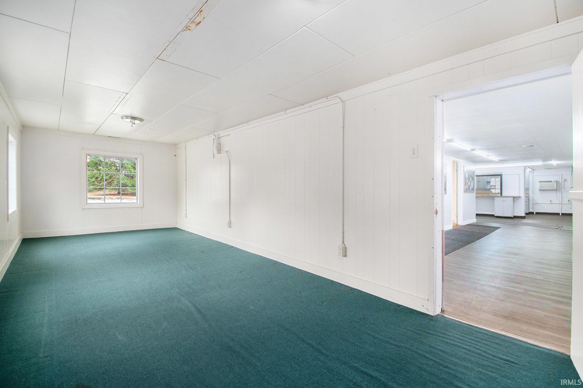 Carpeted empty room featuring baseboards and wood walls