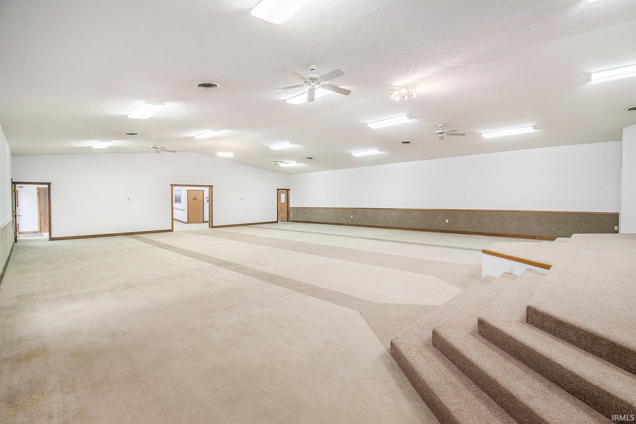 Empty room featuring a ceiling fan, light carpet, lofted ceiling, and a textured ceiling