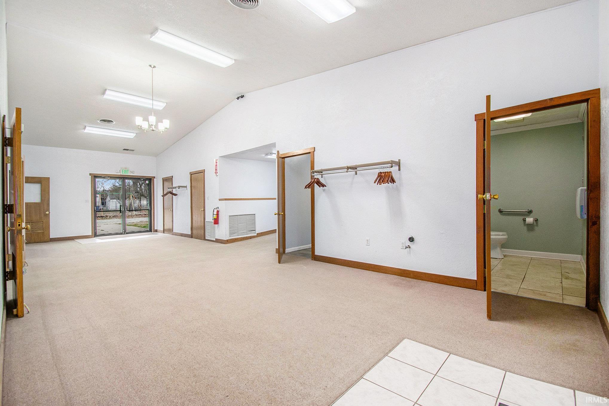 Unfurnished room featuring light colored carpet, vaulted ceiling, light tile patterned flooring, and a chandelier