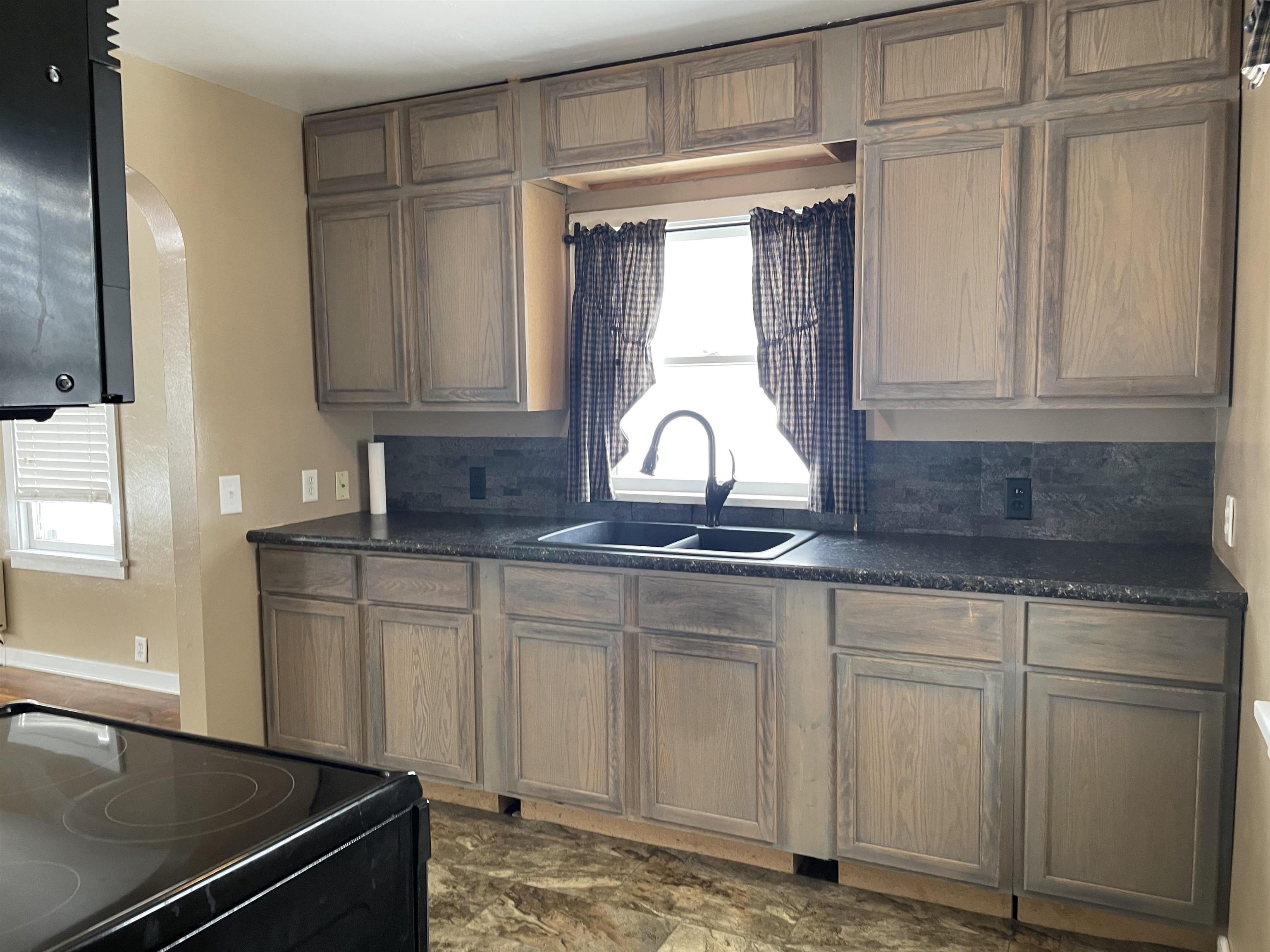 Kitchen with black range with electric stovetop, decorative backsplash, arched walkways, and dark stone countertops