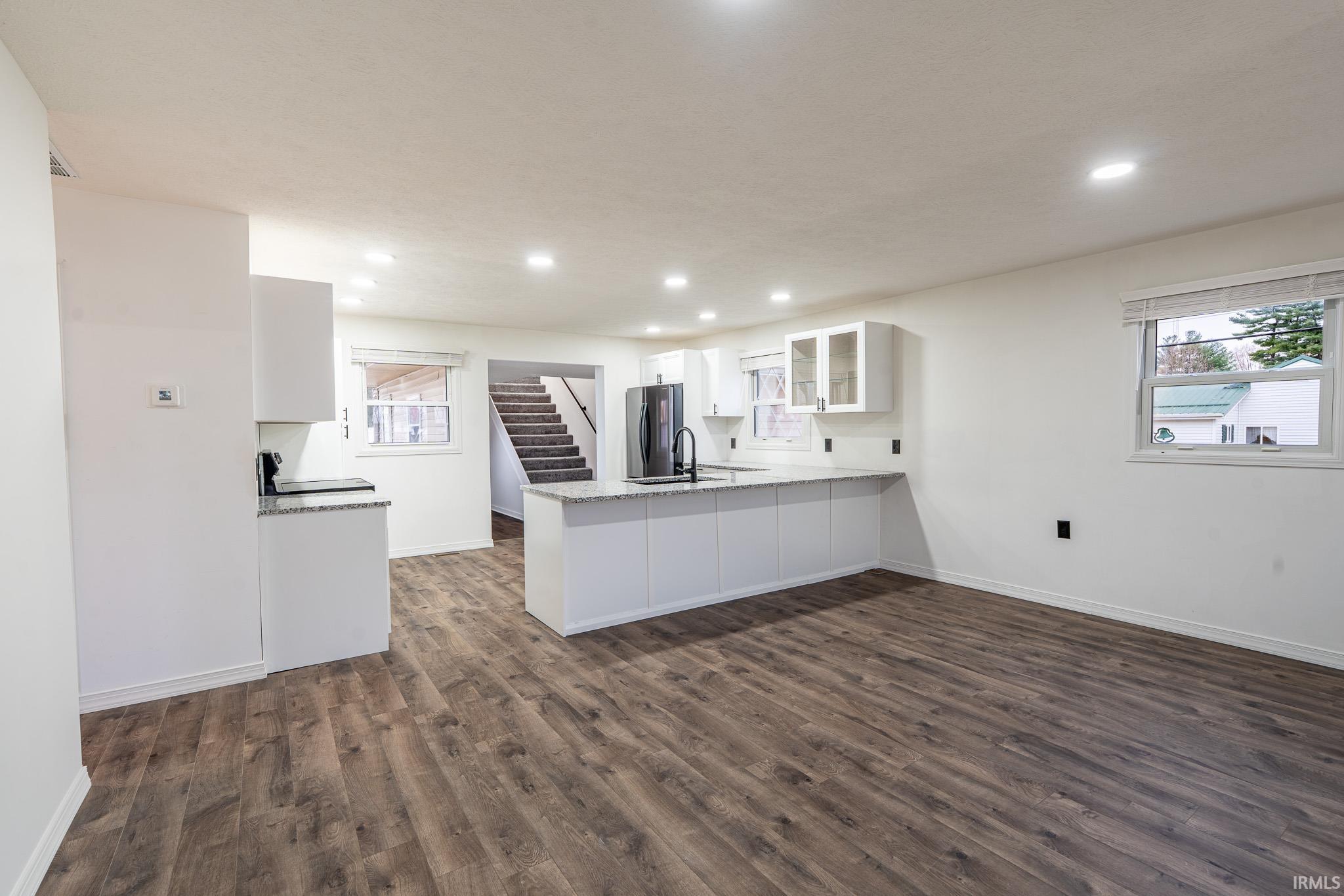 Kitchen featuring white cabinets, a peninsula, glass insert cabinets, dark wood-style floors, and light stone countertops