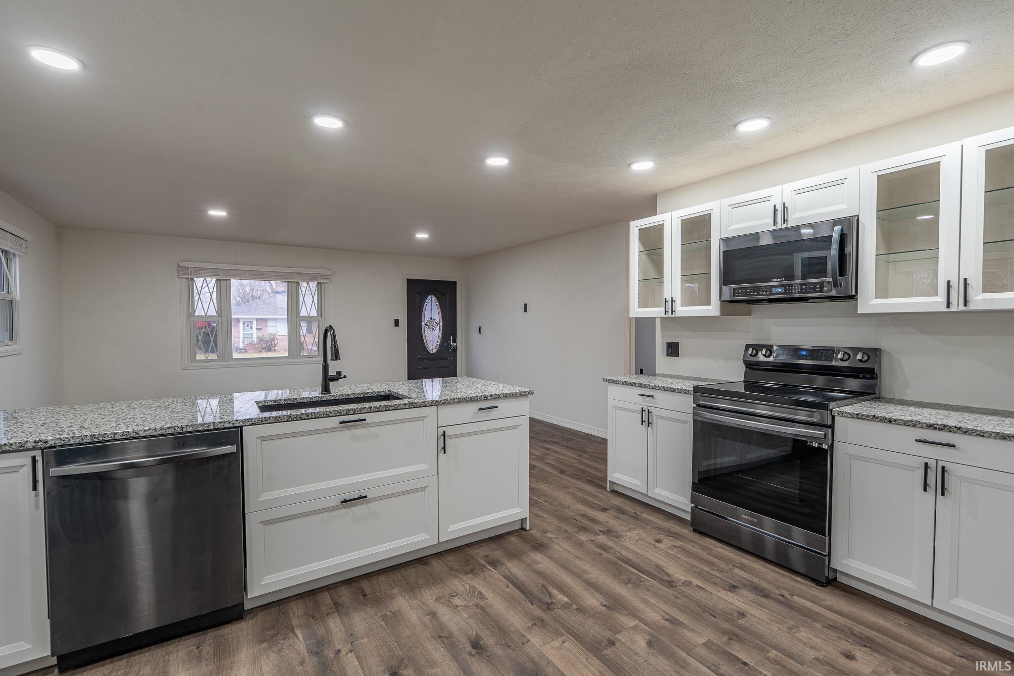Kitchen featuring appliances with stainless steel finishes, white cabinetry, recessed lighting, light stone countertops, and glass insert cabinets