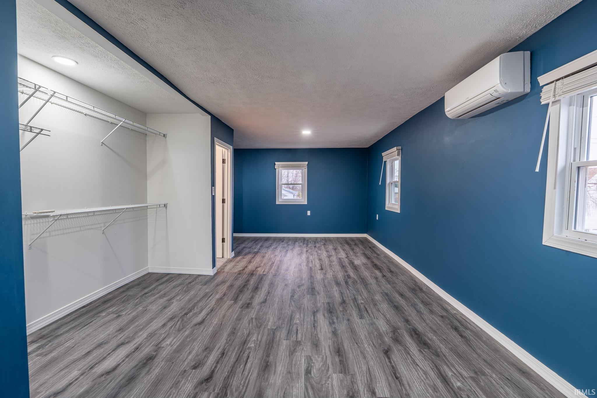 Unfurnished bedroom with a textured ceiling, dark wood-type flooring, and a wall mounted air conditioner