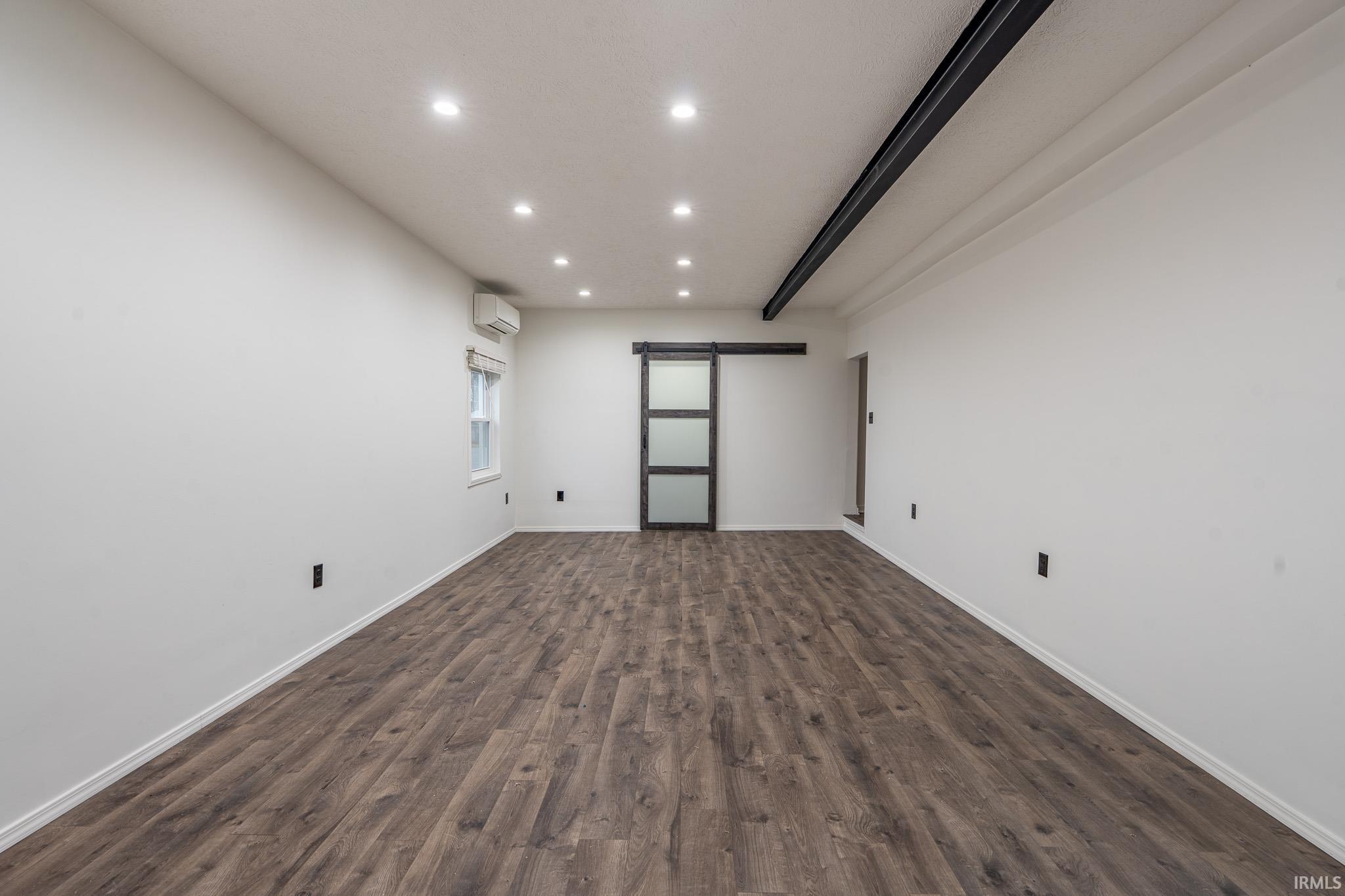 Unfurnished room with a barn door, recessed lighting, and dark wood-style floors