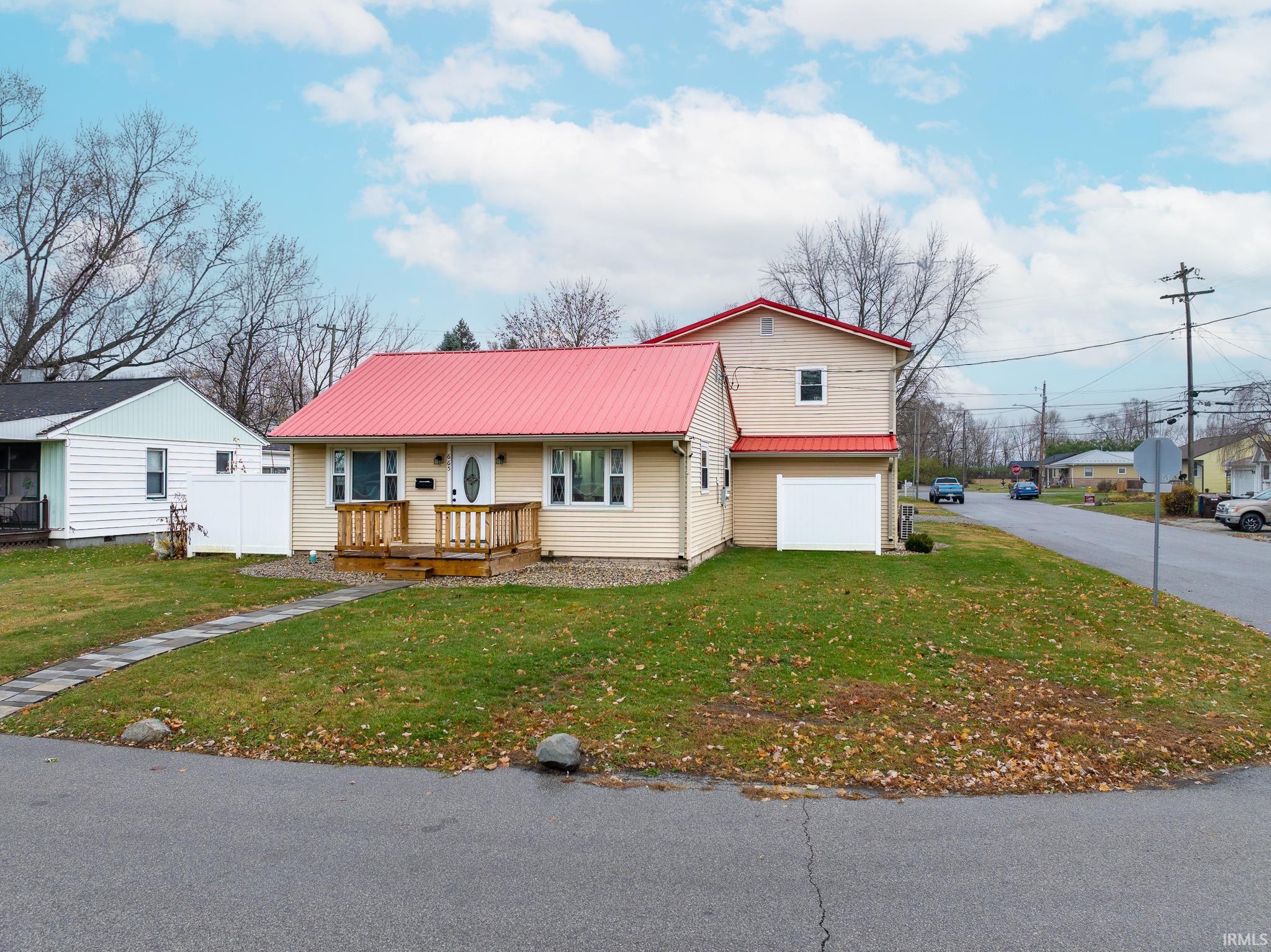 View of front of home with a garage, a metal roof, a front lawn, and a wooden deck