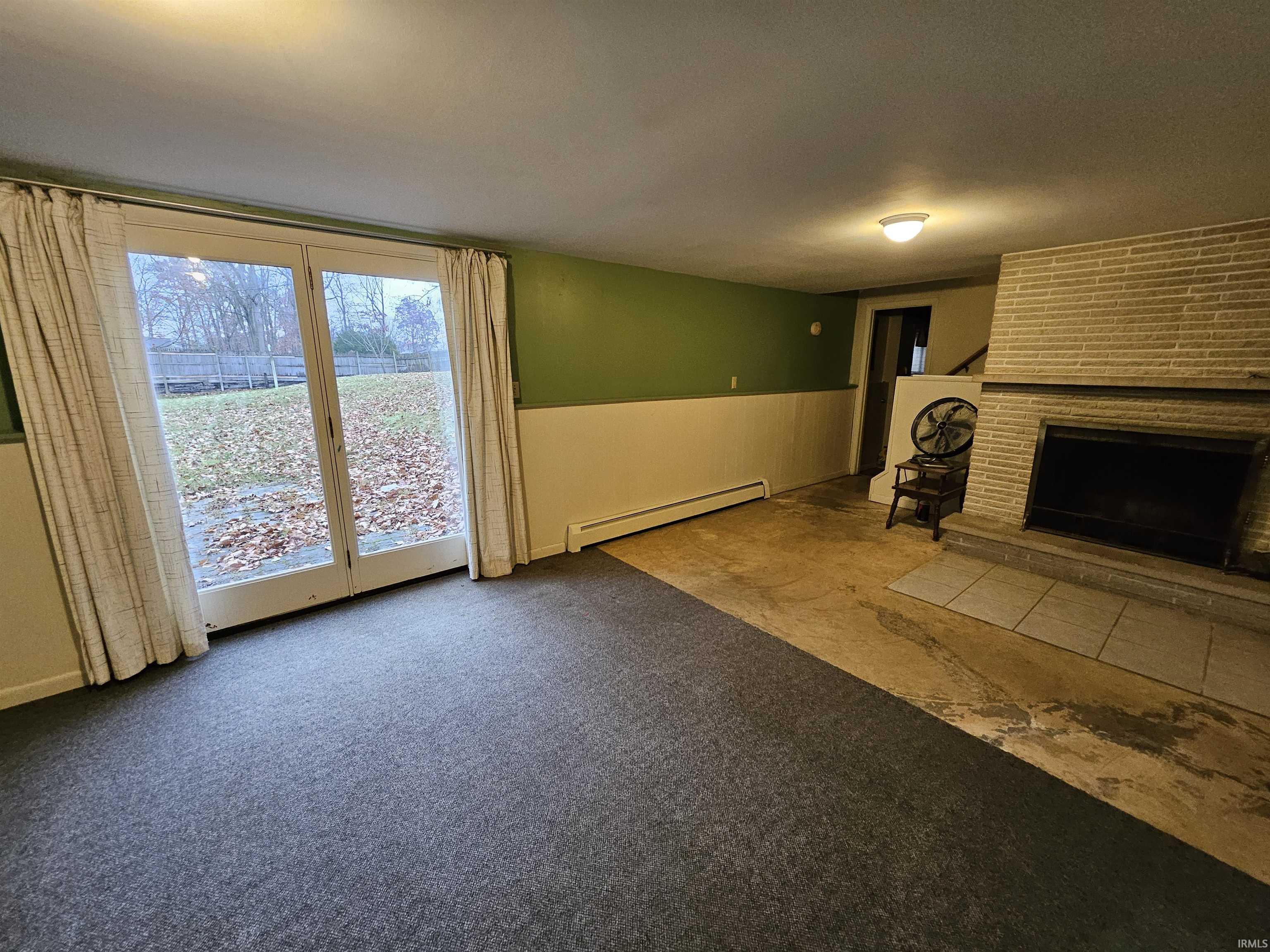 Unfurnished living room featuring carpet, a fireplace, a baseboard heating unit, and wainscoting