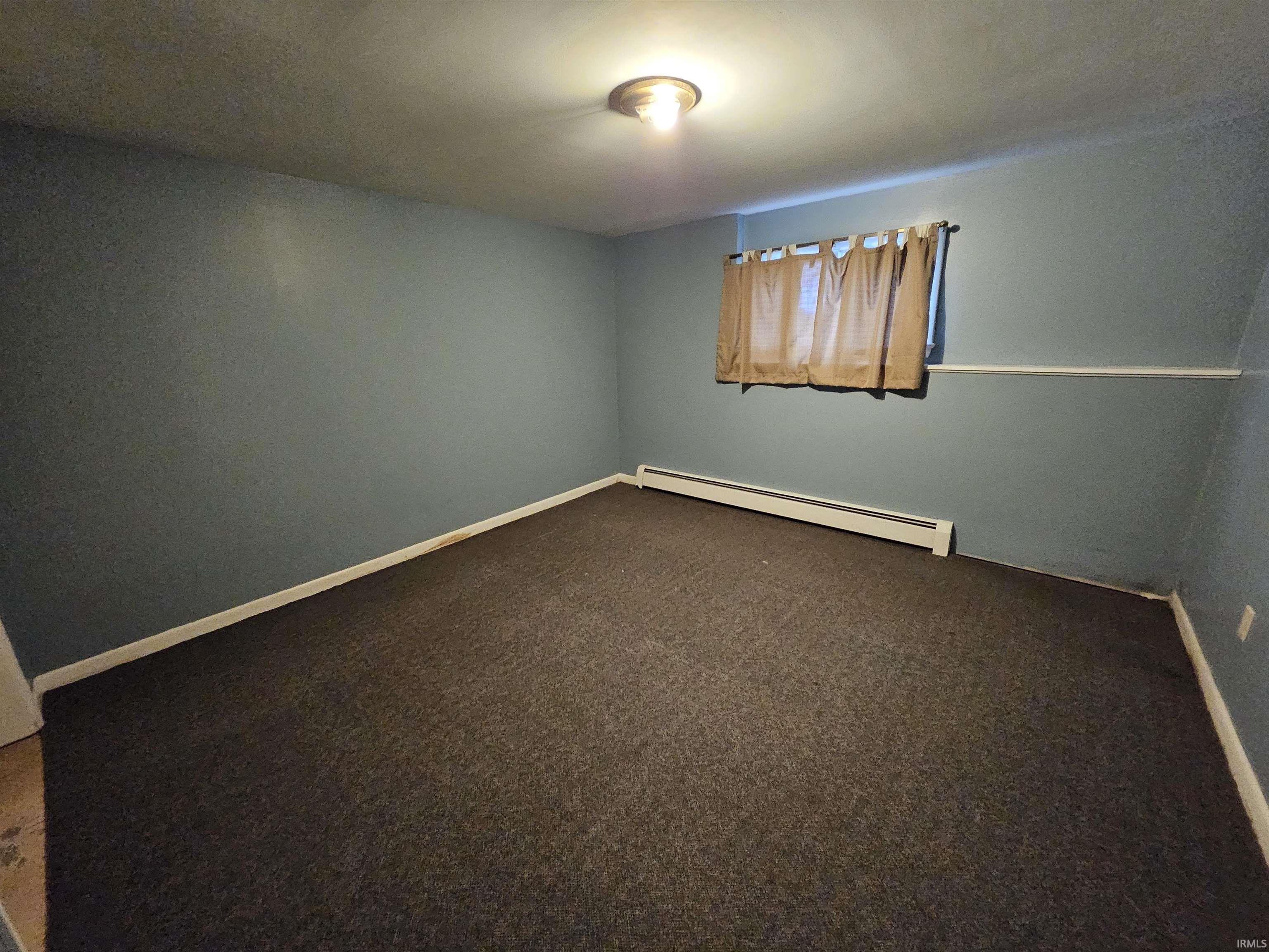 Spare room with a baseboard heating unit and dark colored carpet