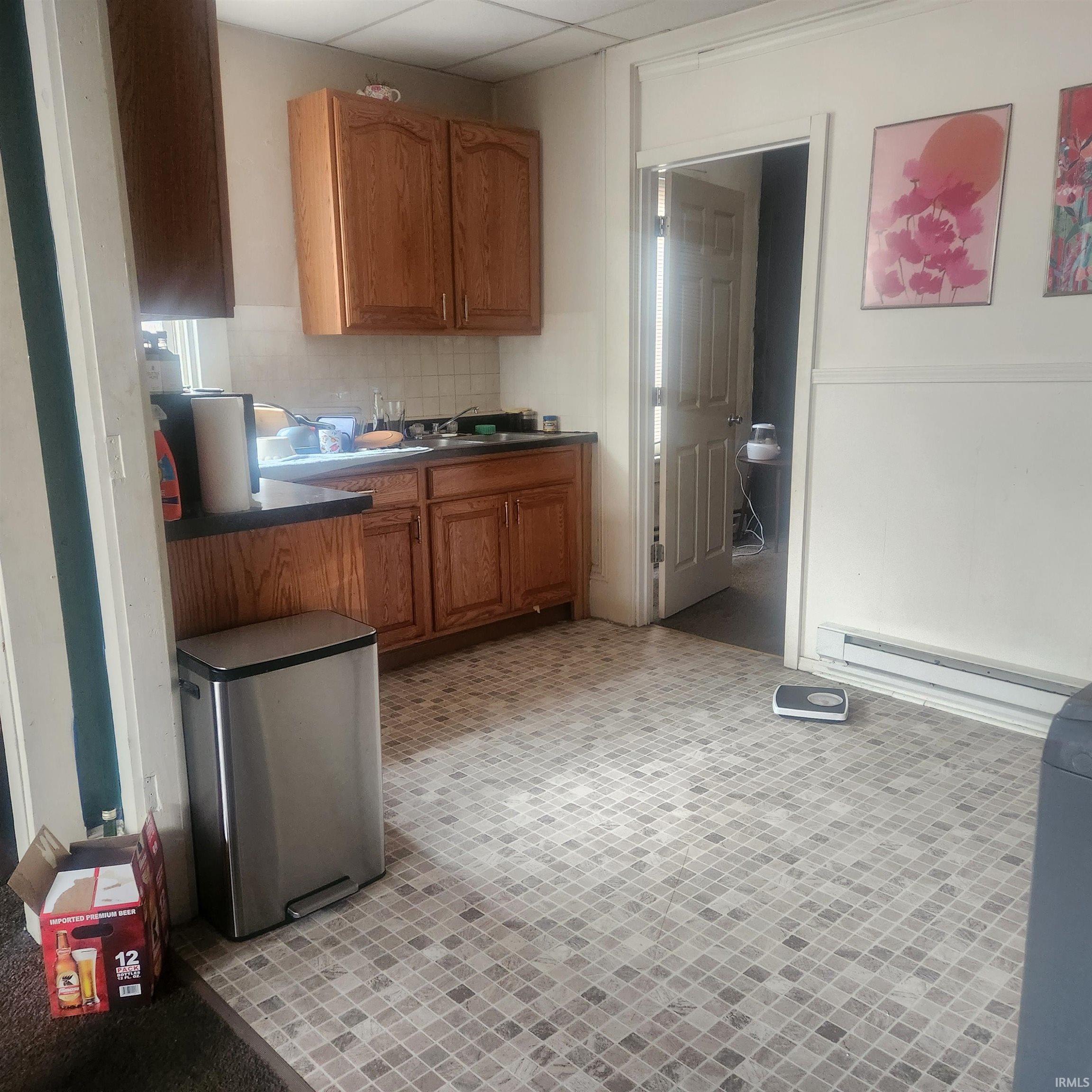 Kitchen featuring stainless steel fridge, brown cabinetry, a drop ceiling, decorative backsplash, and a baseboard heating unit