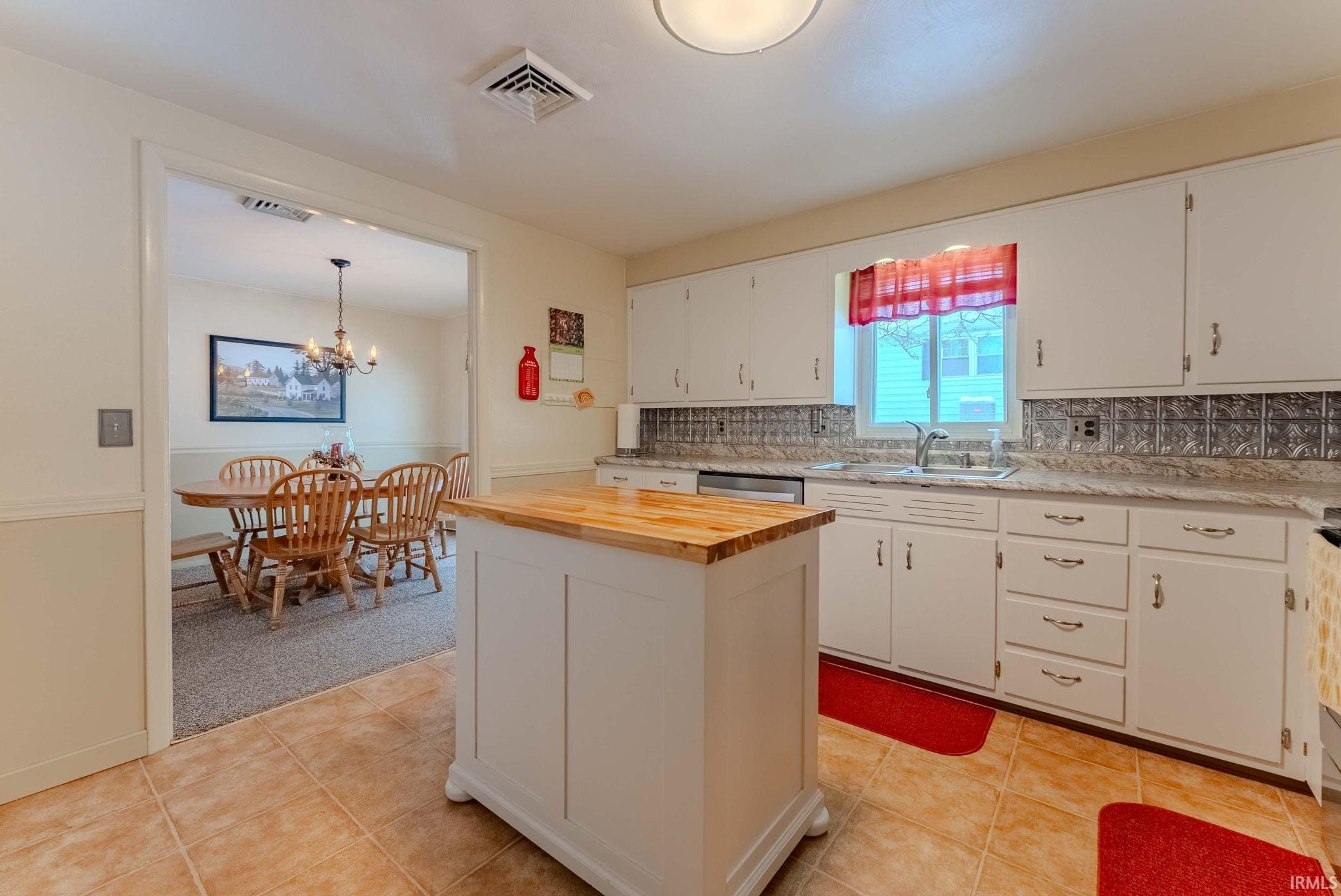 Kitchen with wooden counters, a chandelier, tasteful backsplash, white cabinets, and light tile patterned flooring