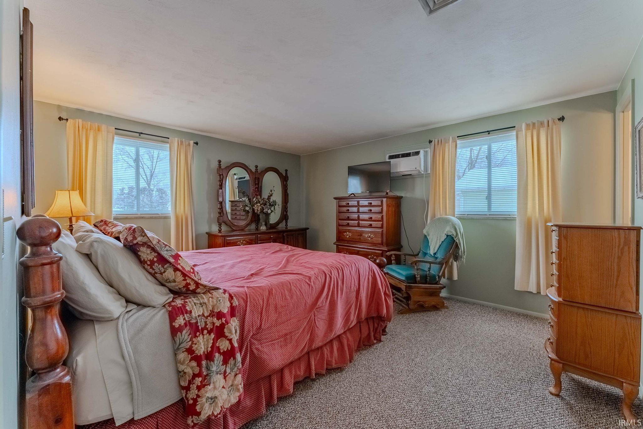 Bedroom featuring carpet floors, multiple windows, and a wall mounted air conditioner