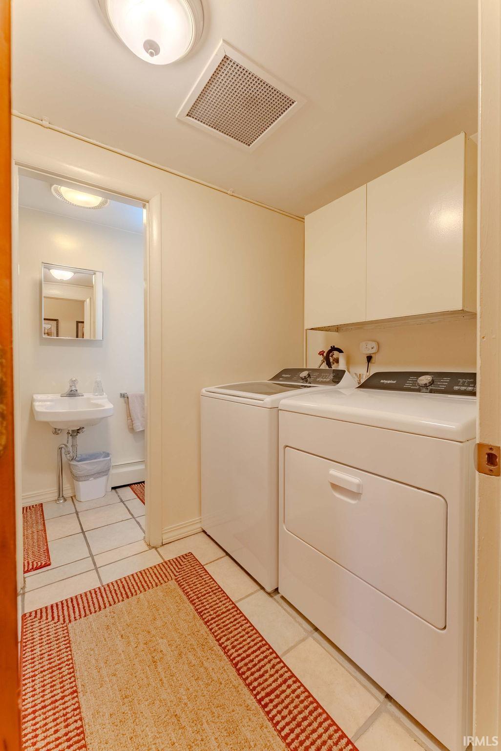 Laundry room with independent washer and dryer, light tile patterned floors, and cabinet space