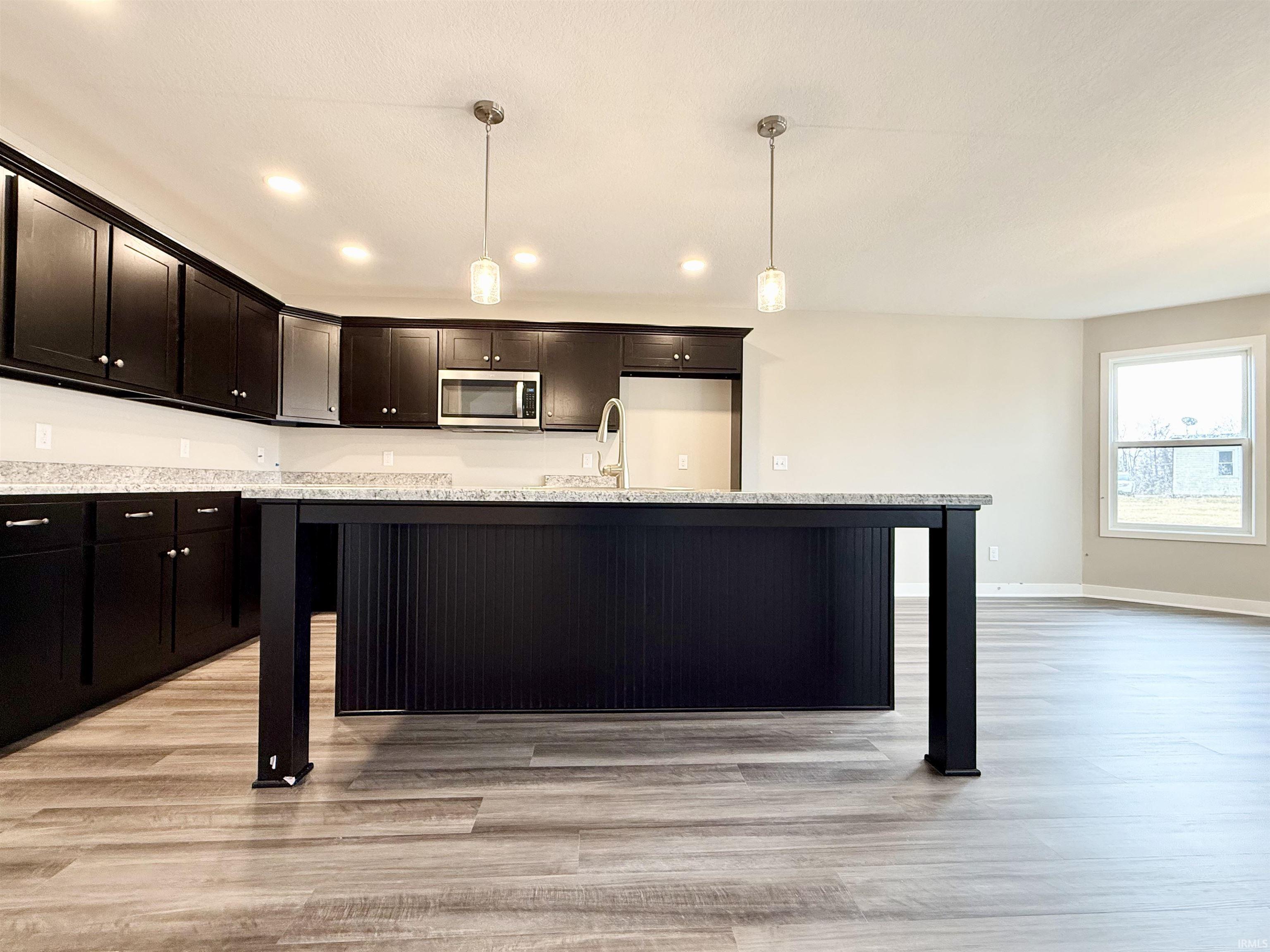 Kitchen featuring a kitchen bar, a center island with sink, hanging light fixtures, and light wood-style flooring