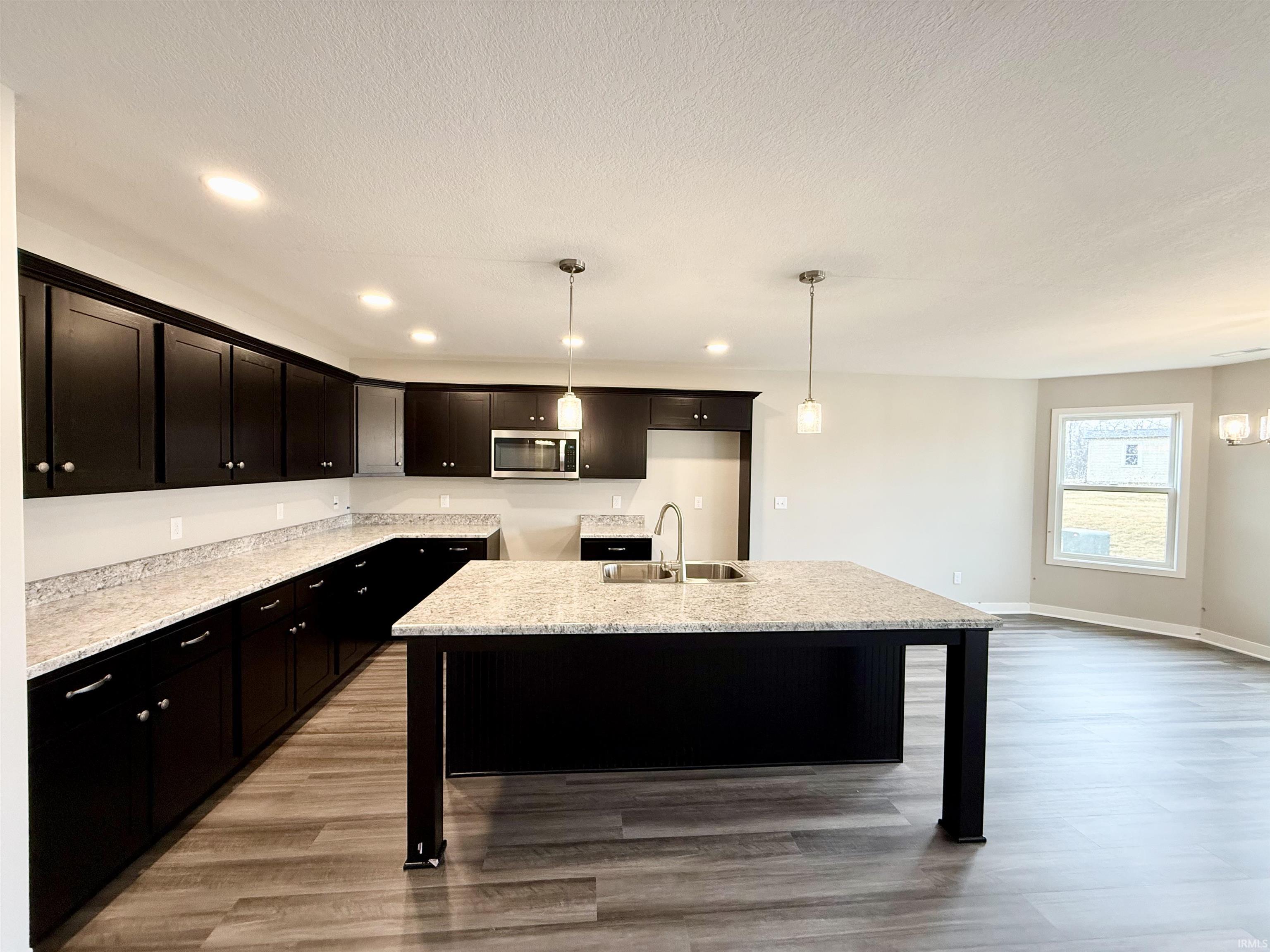 Kitchen with light stone counters, a center island with sink, a kitchen breakfast bar, light wood finished floors, and a textured ceiling