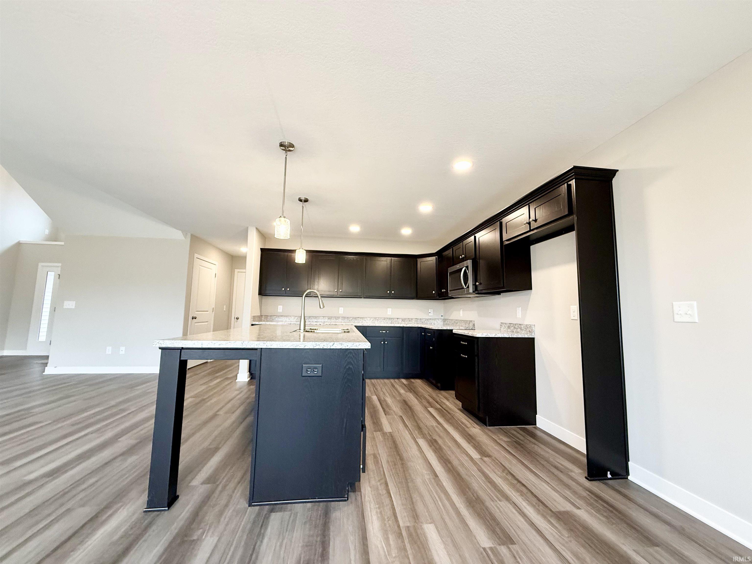 Kitchen with light wood-type flooring, a kitchen bar, pendant lighting, a kitchen island with sink, and light stone countertops